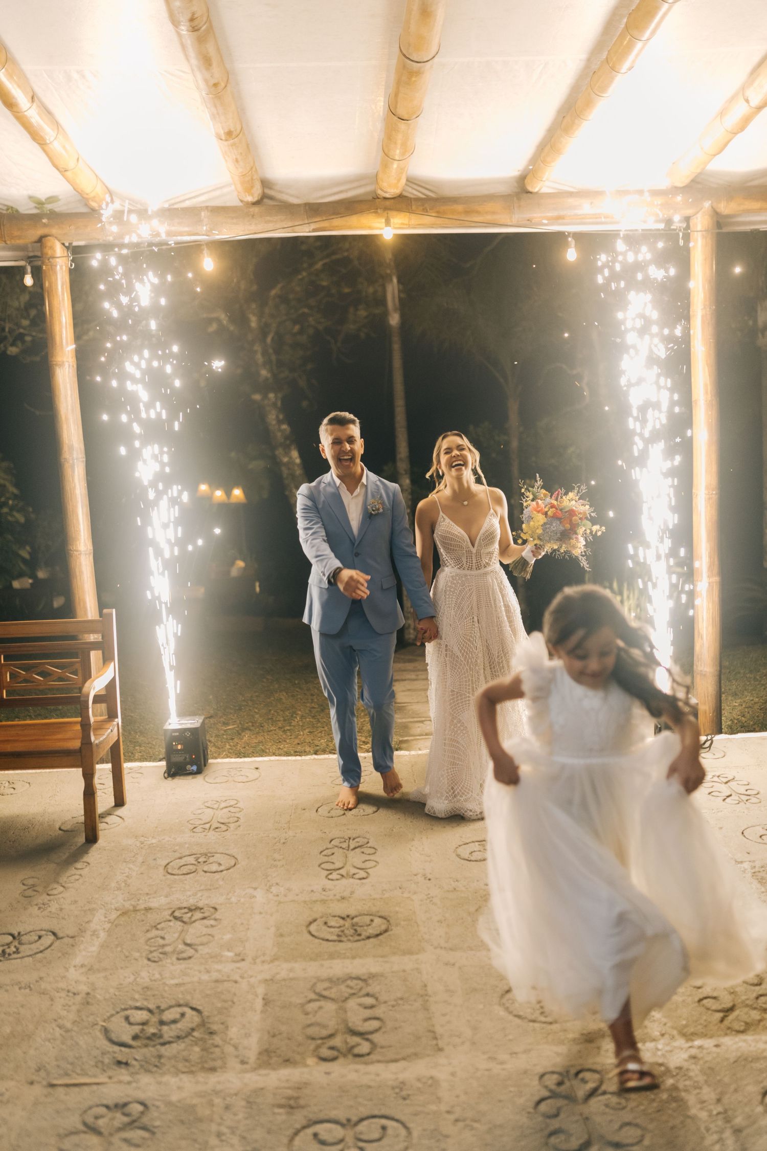 Wedding party dancing and celebrating under sparklers and string lights on outdoor covered patio.
