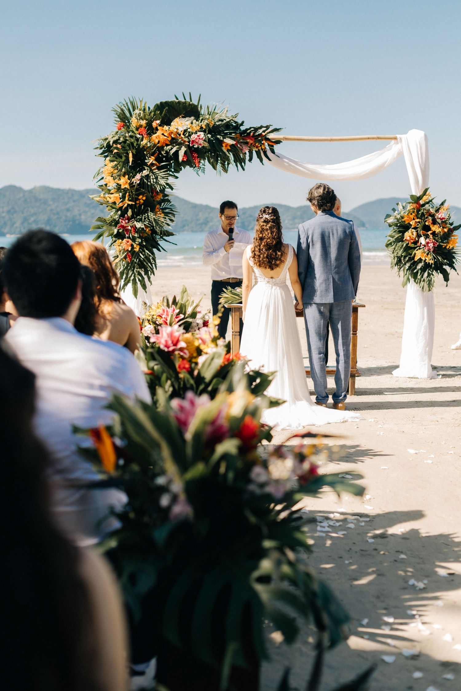 A beautiful beach wedding ceremony setup with tropical floral arrangements and white fabric arch.