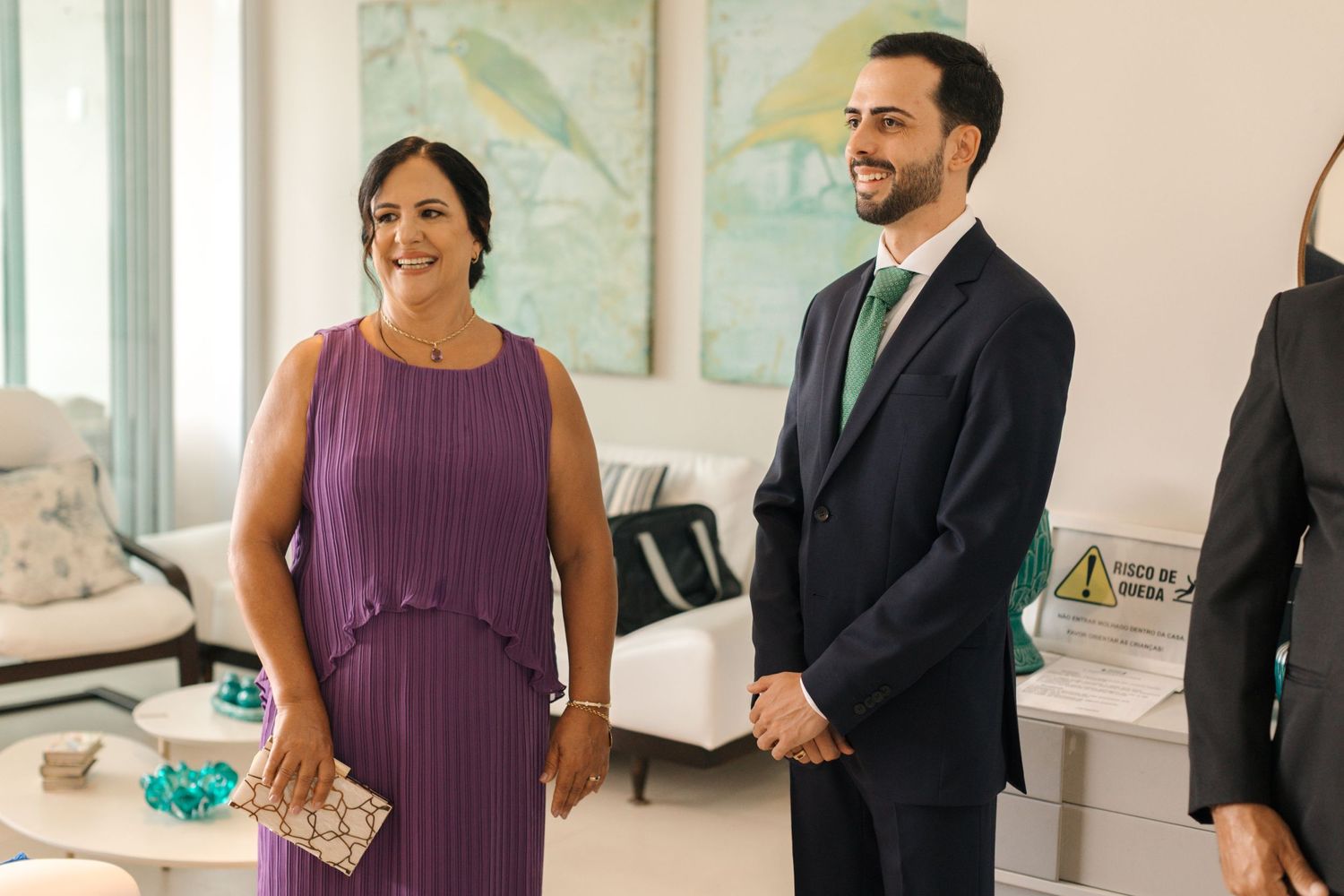 Wedding guests in formal attire smile during pre-ceremony gathering in bright indoor space.