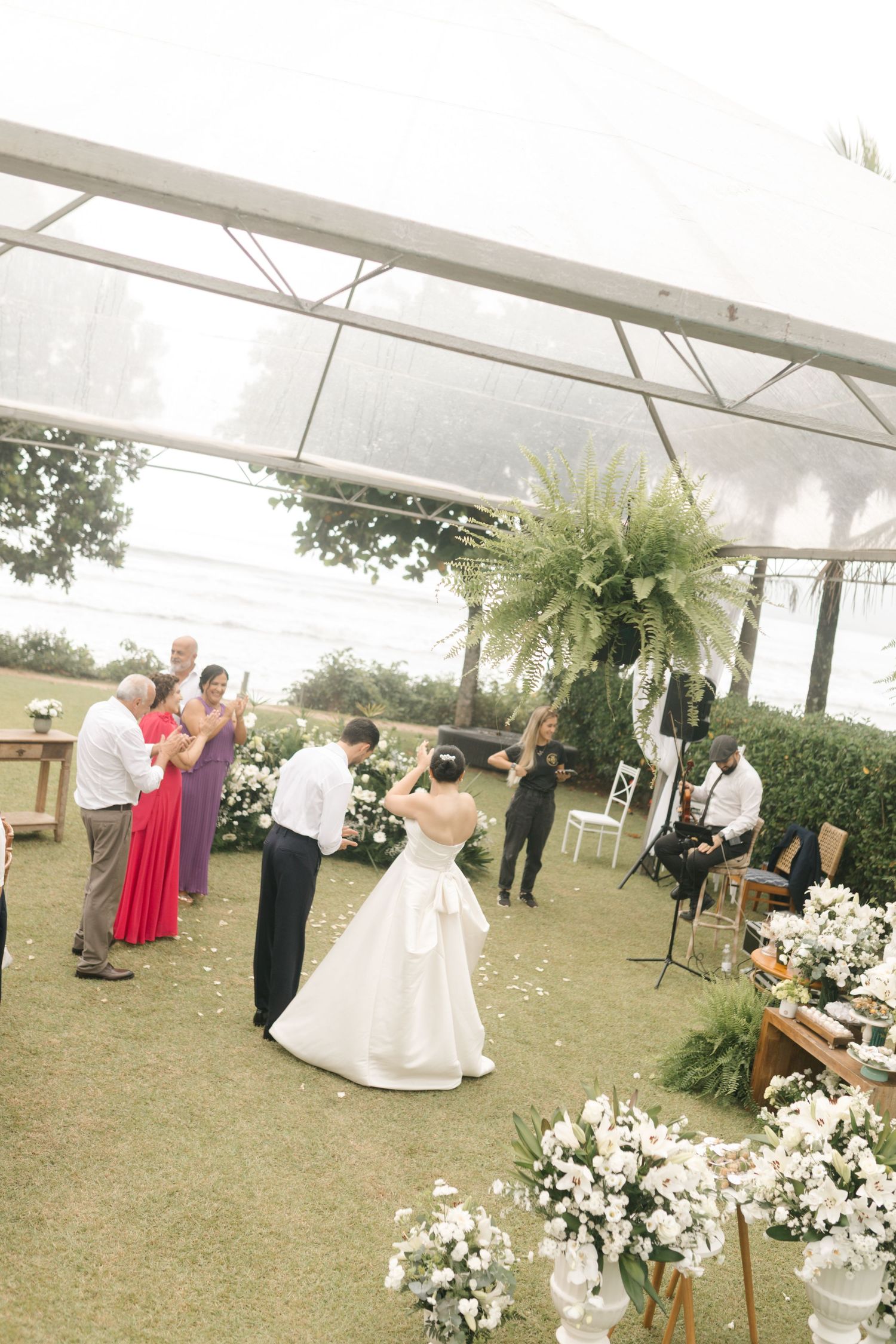 Outdoor wedding reception with floral decorations and guests dancing under a white tent.