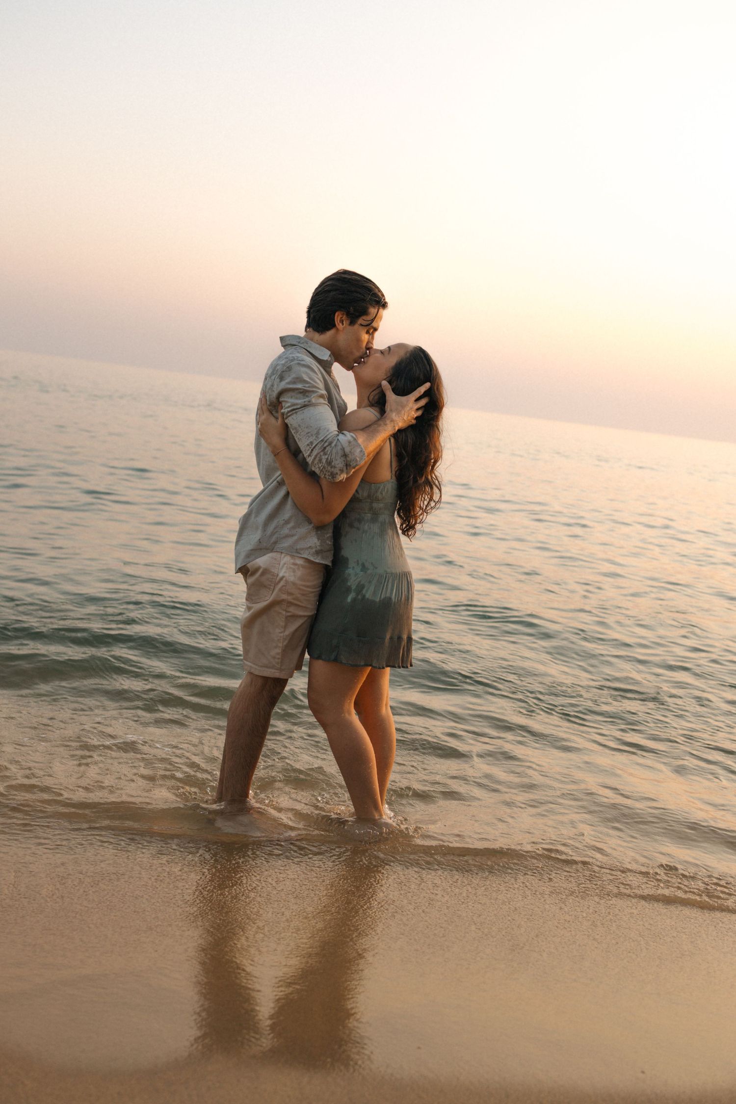 Dancing couple silhouetted against sunset over ocean waves at beach.