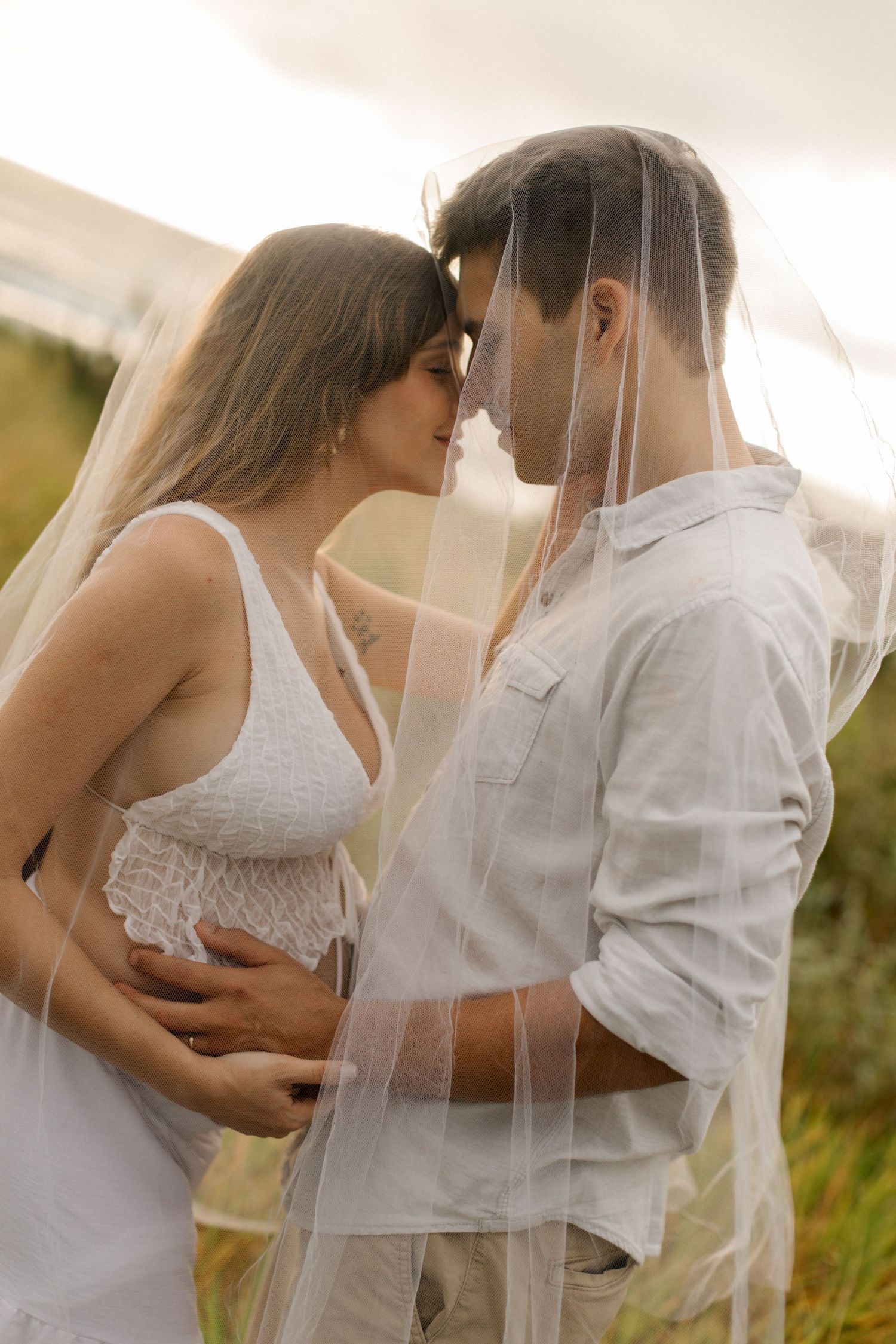 Romantic couple sharing an intimate moment under a veil in a sunlit outdoor setting.