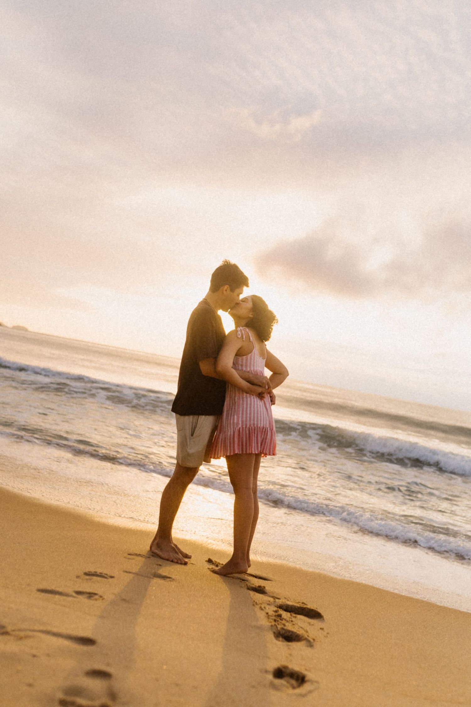 m casal romântico em pé em uma praia ao pôr do sol deixando pegadas na areia.