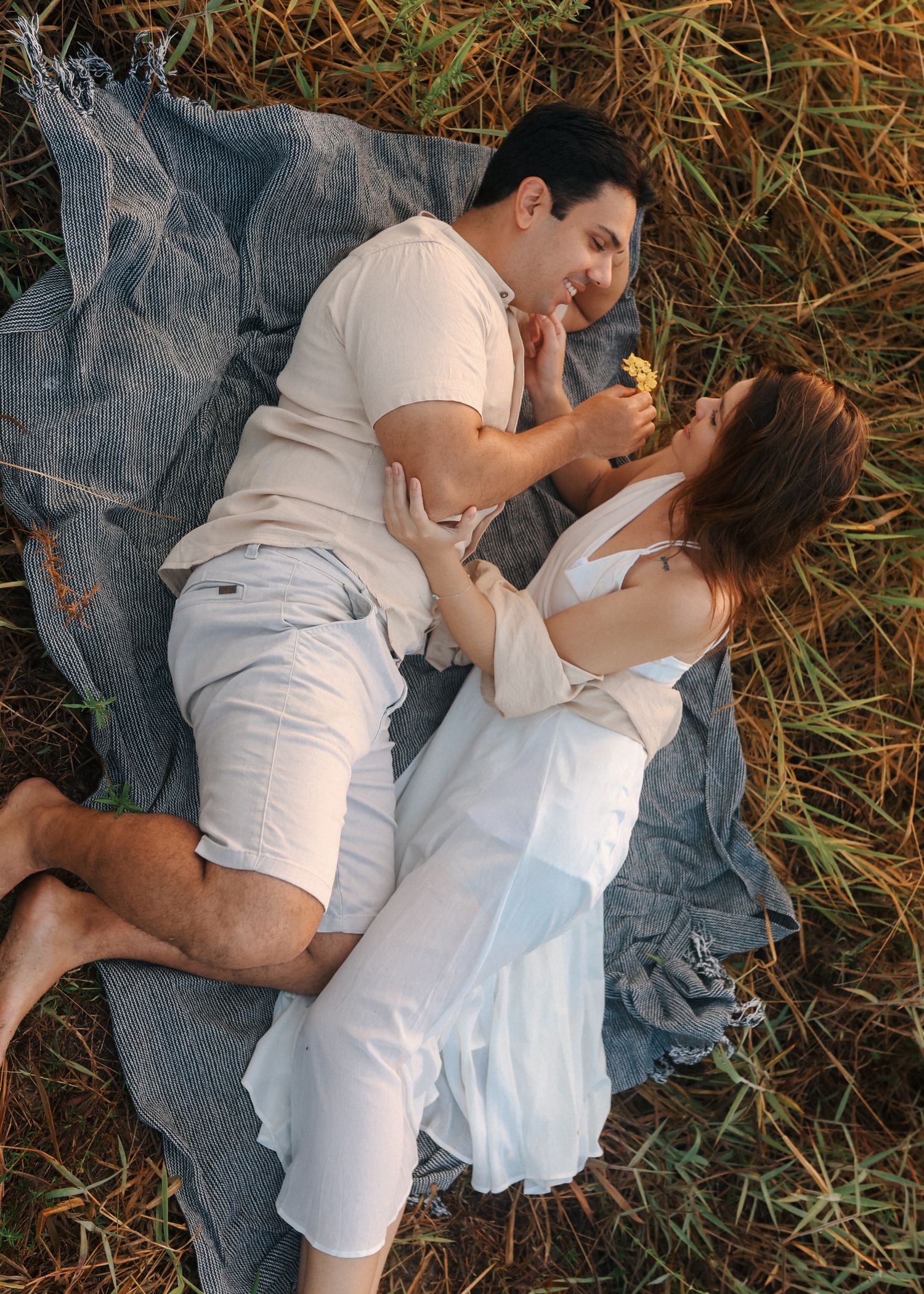 Intimate couple poses on blue blanket surrounded by tall grass at sunset.