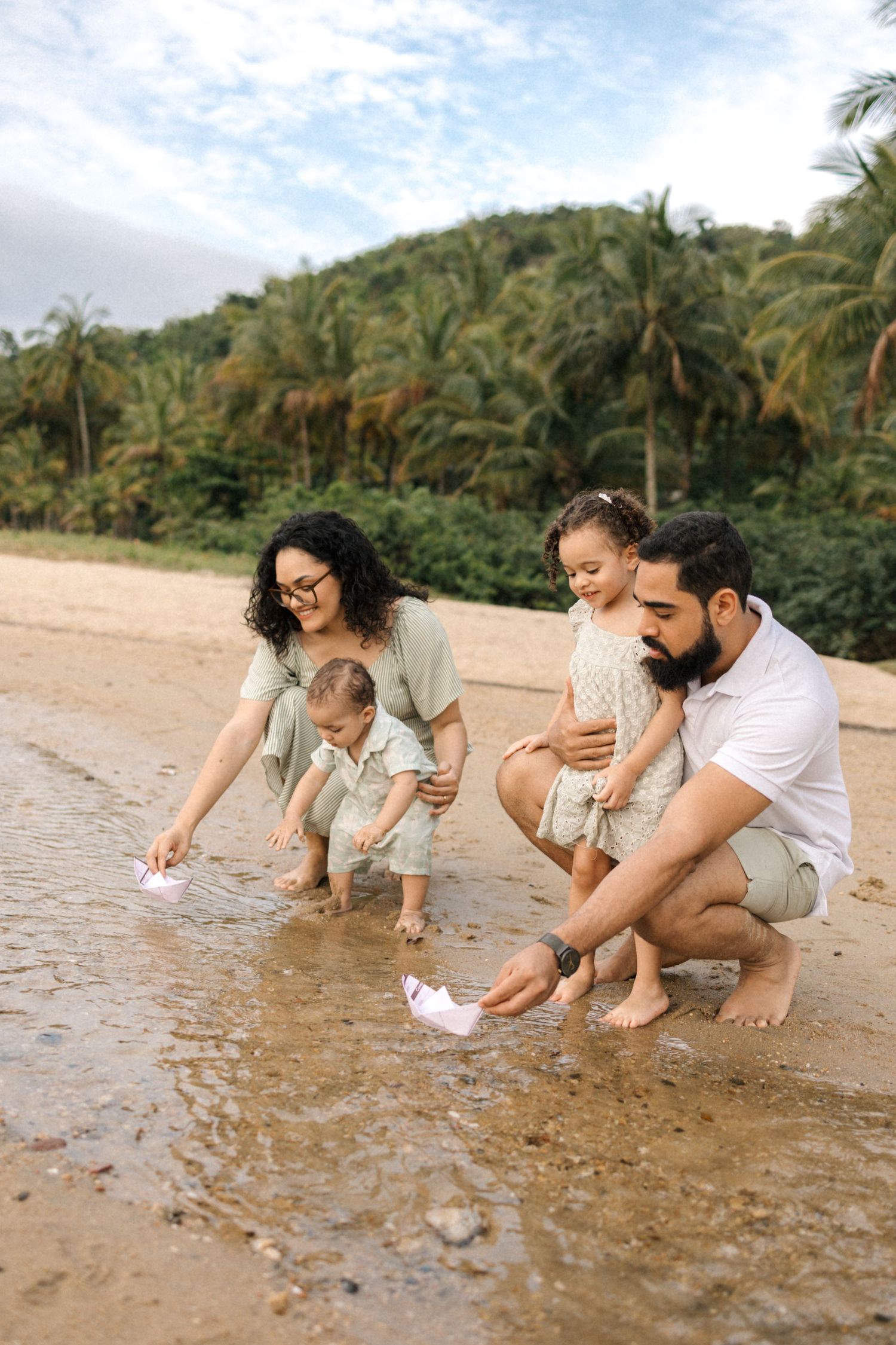 Family enjoying time together searching for seashells on a tropical beach with palm trees in the background.