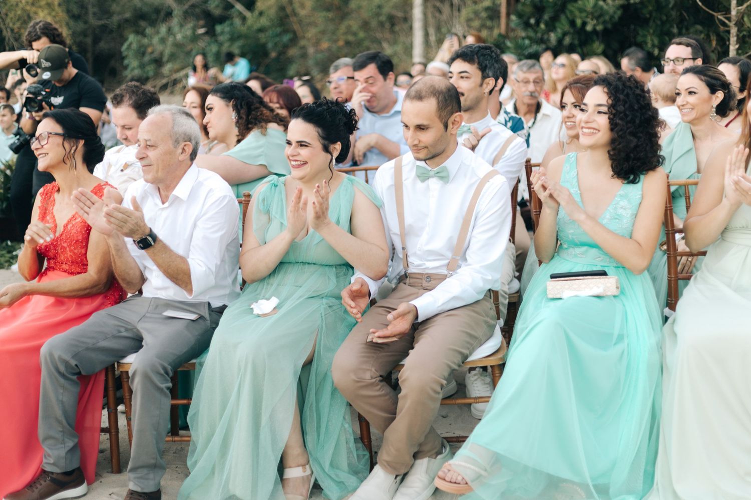 Wedding guests in coral and mint dresses react emotionally during ceremony.