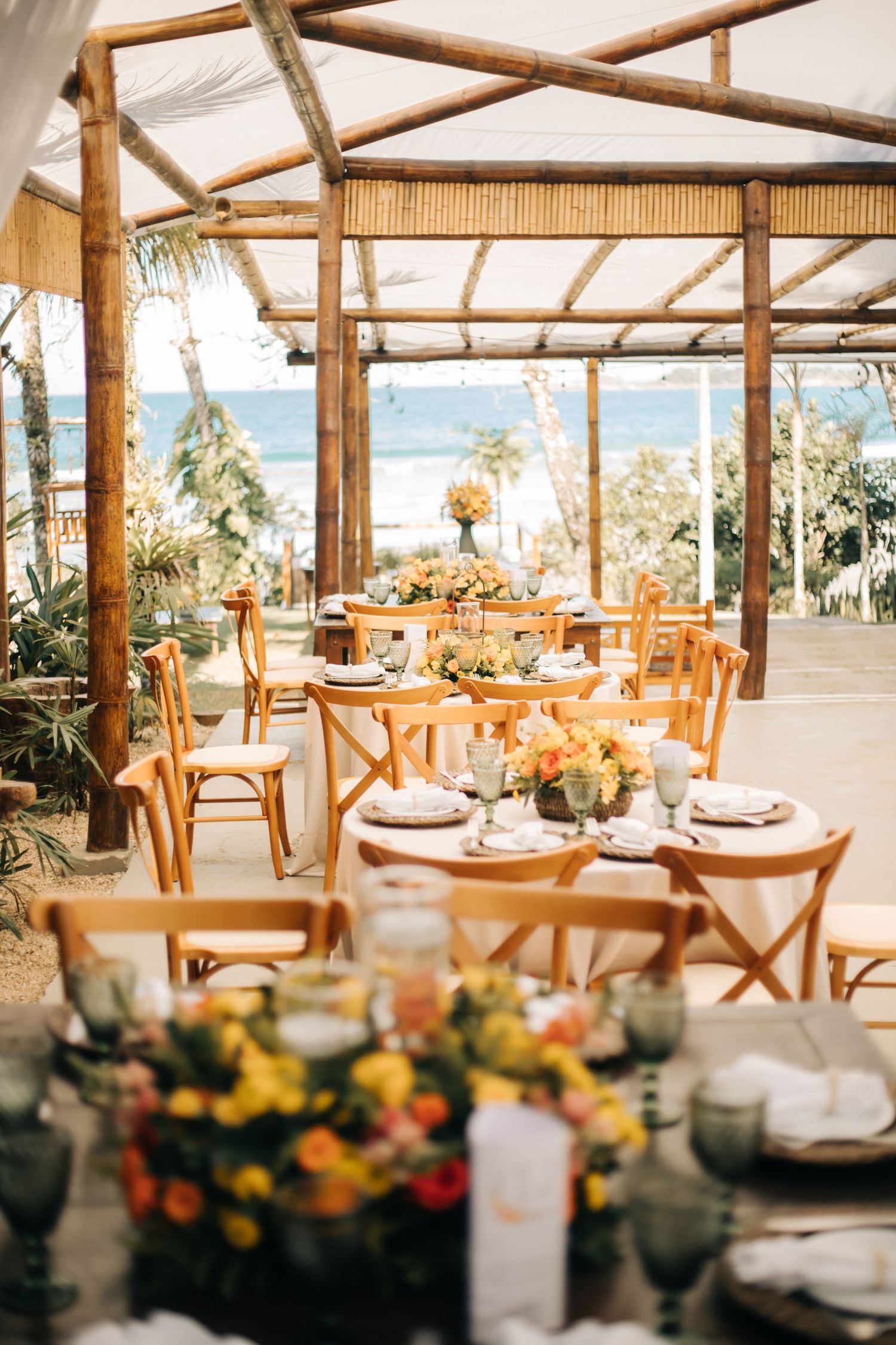 Tropical wedding reception venue with bamboo framework and elegant table settings overlooking the ocean.