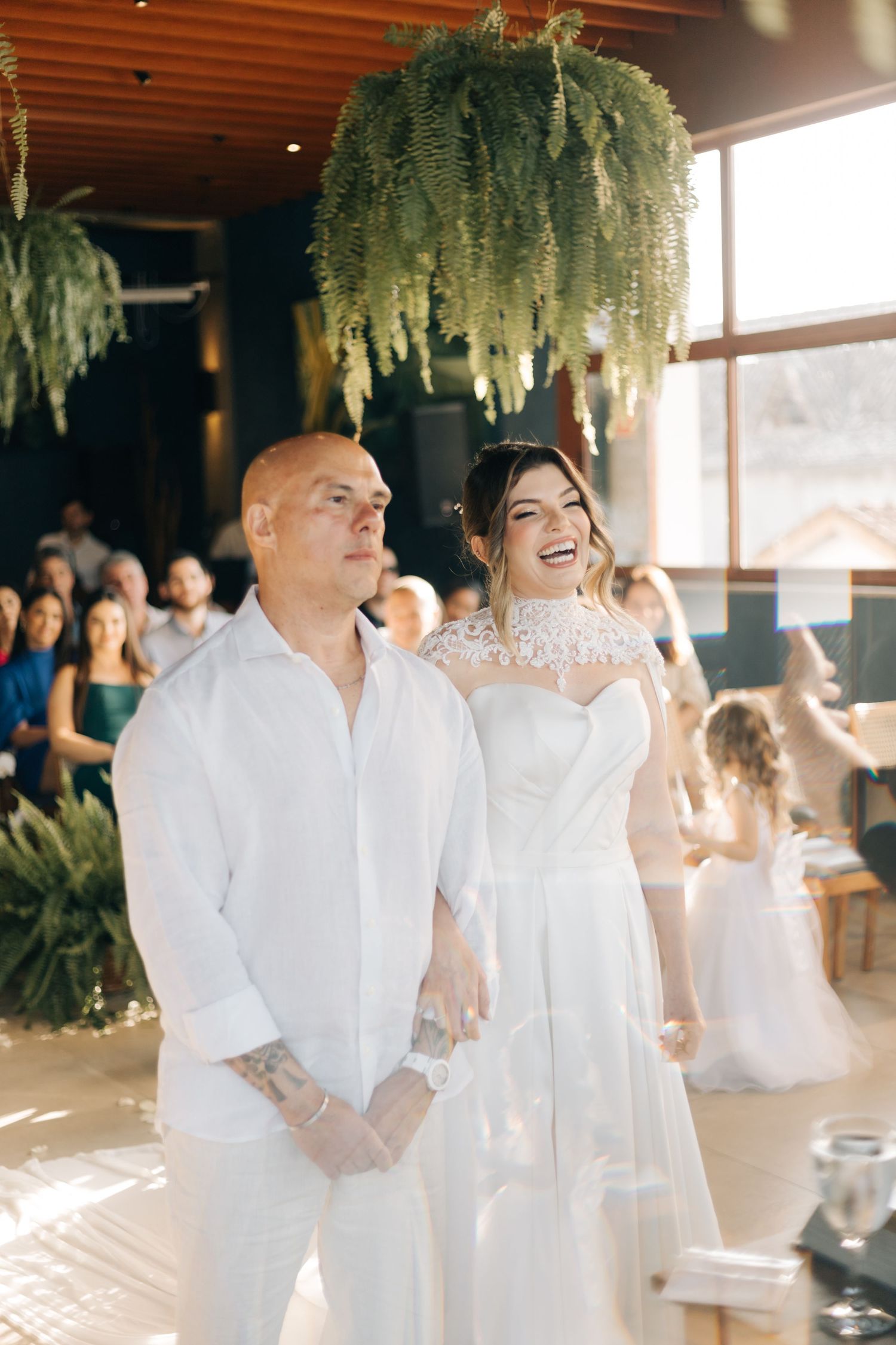 Wedding celebration in a bright indoor venue with greenery and hanging ferns.