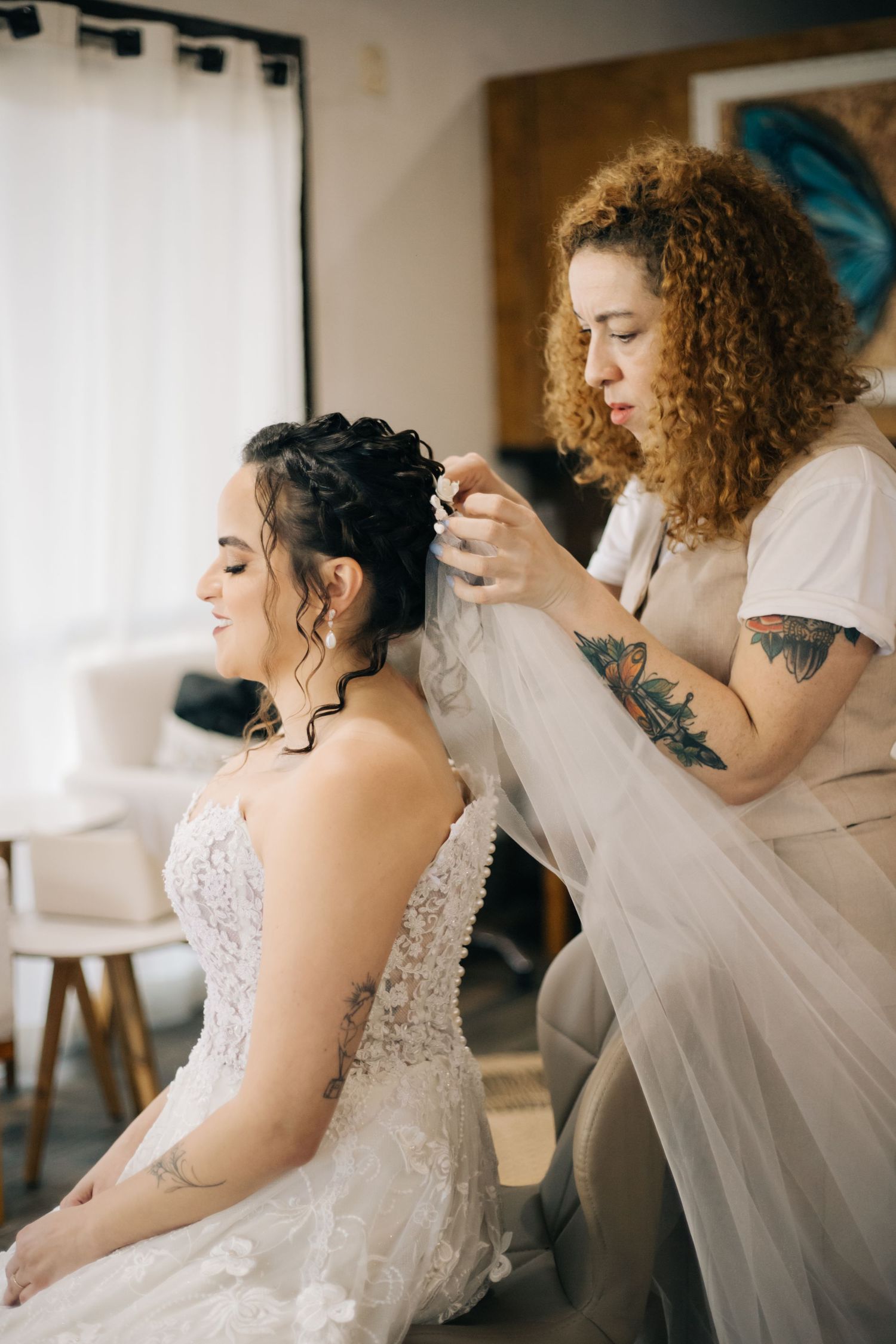 Wedding preparation scene showing stylist adjusting bridal veil and hair.