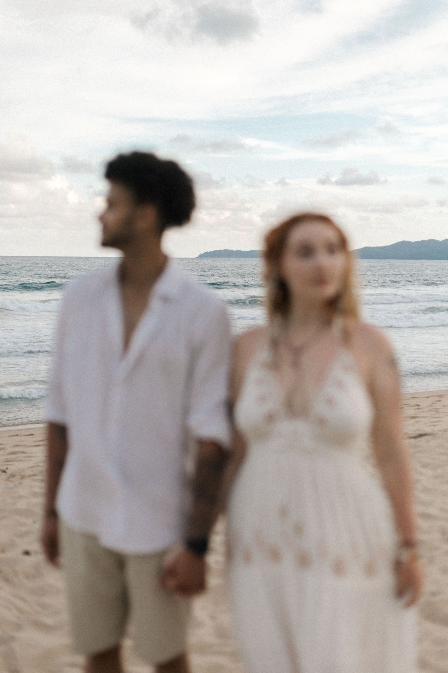 Couple walking along the shoreline in coordinated white and beige beach attire.