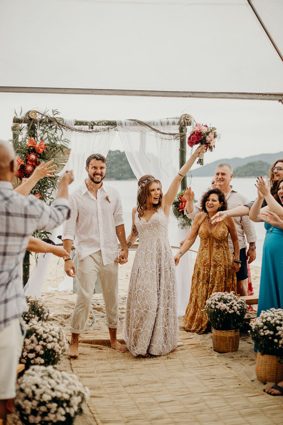 Wedding guests dance and celebrate under a white tent at an outdoor reception.