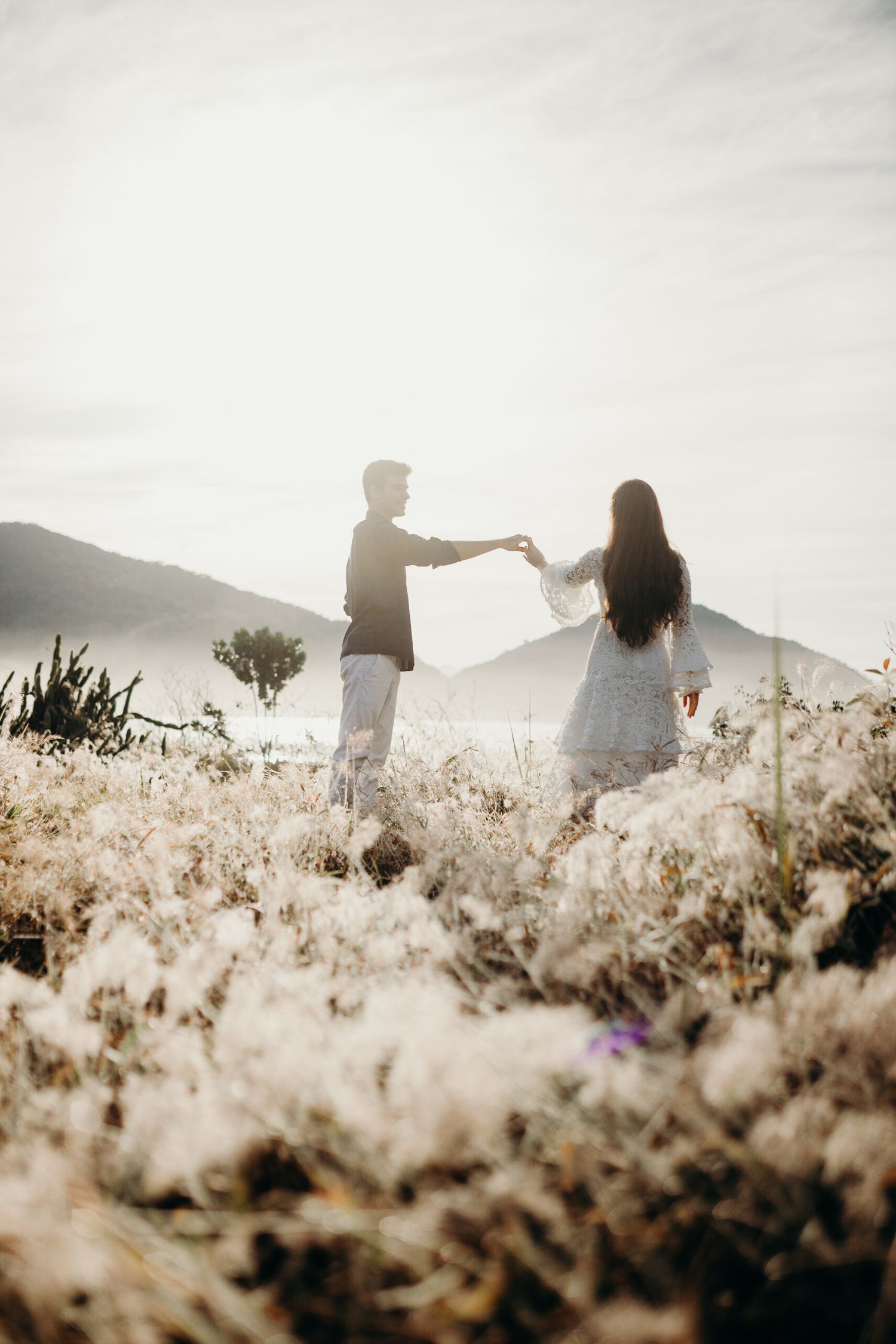 Couple dancing in a field of sunlit grass with mountains in background.