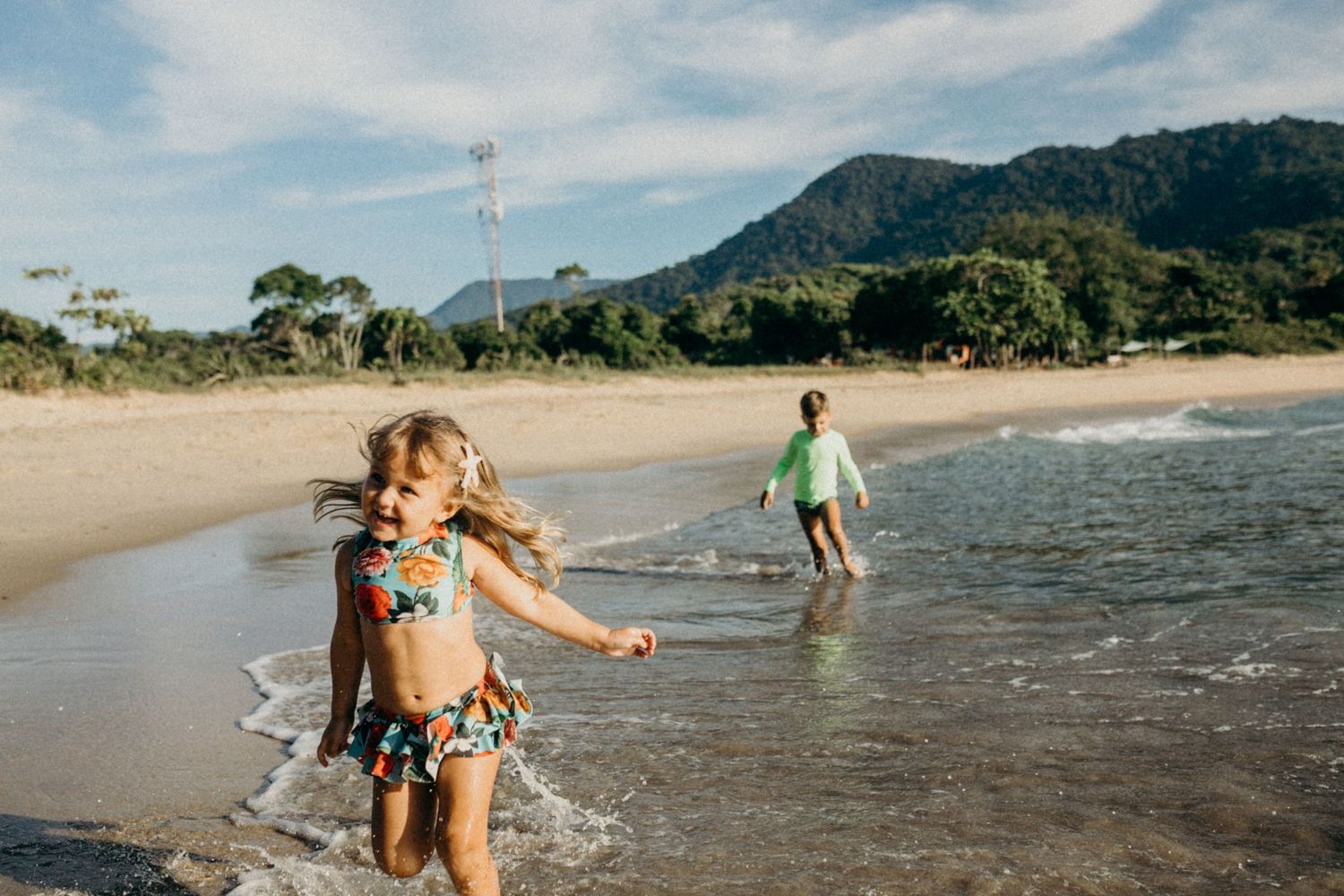 Family playing and splashing together in shallow ocean water with mountains in background.