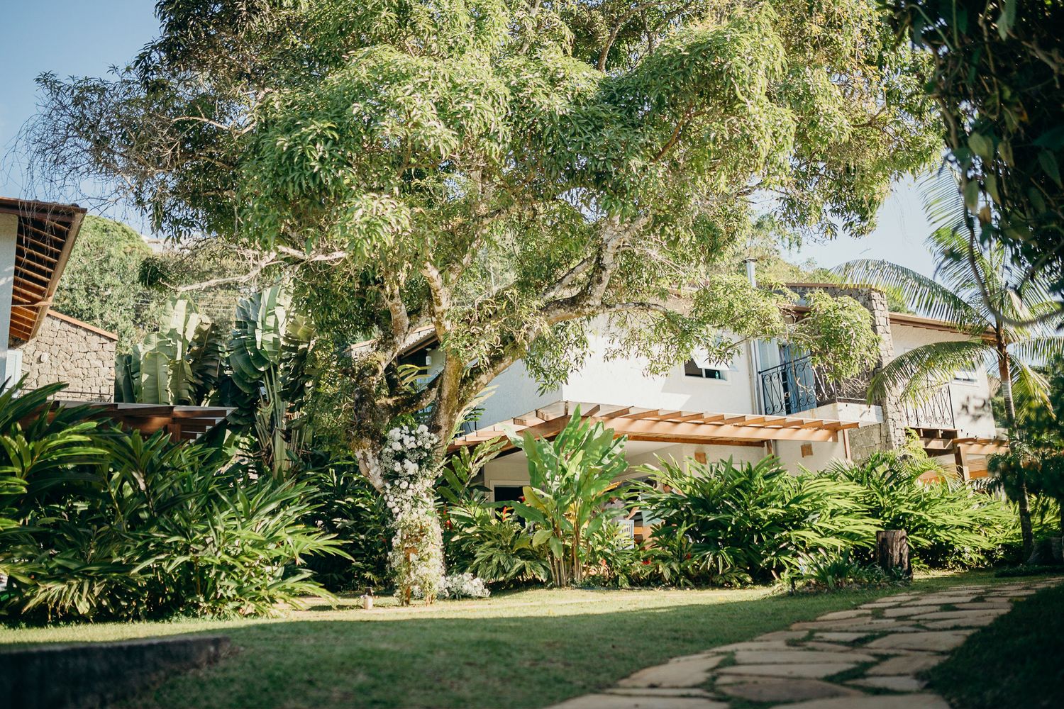 White residential building surrounded by mature trees and manicured tropical gardens.