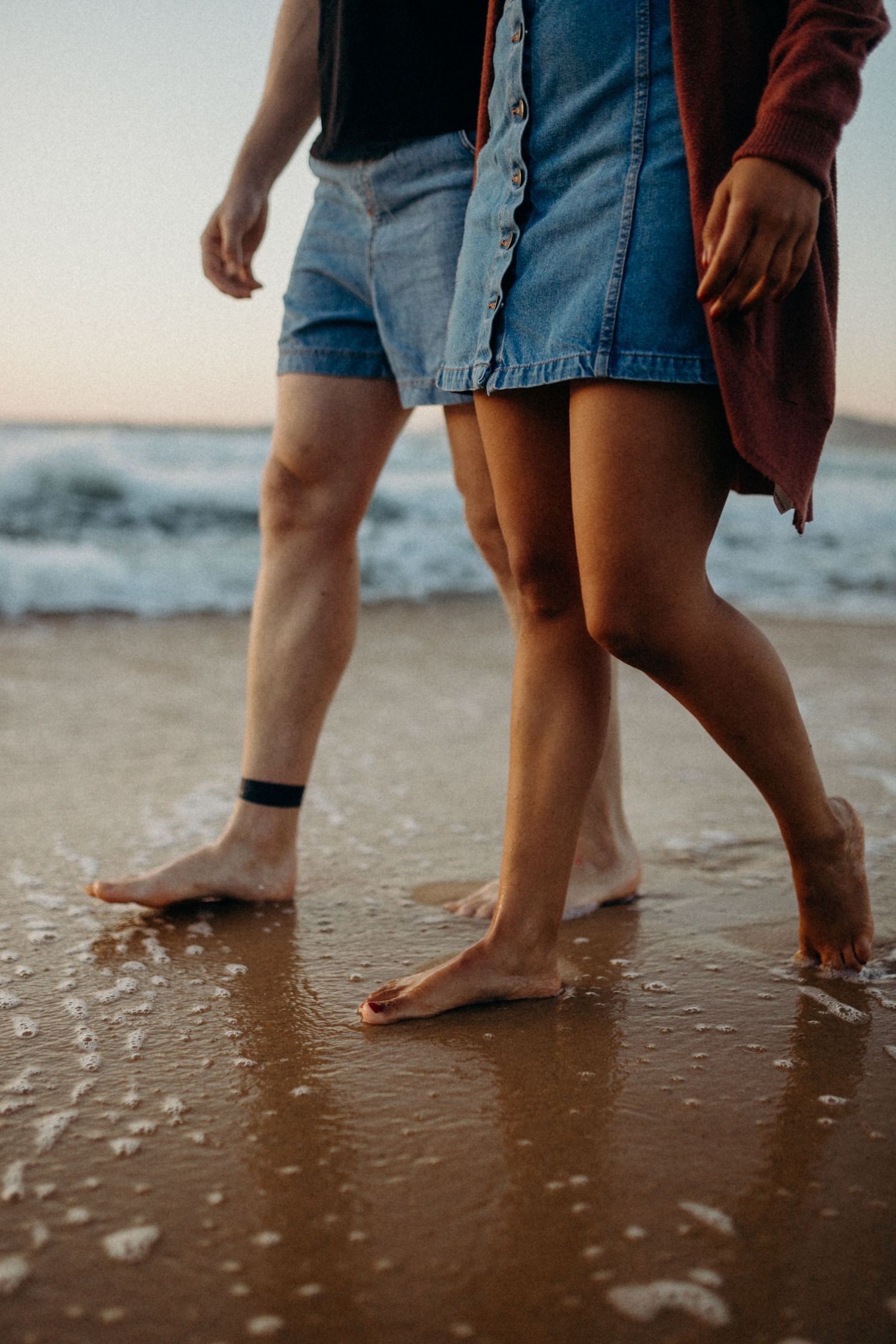 Bare feet walking along the wet sand at the beach during sunset with gentle waves washing over them.