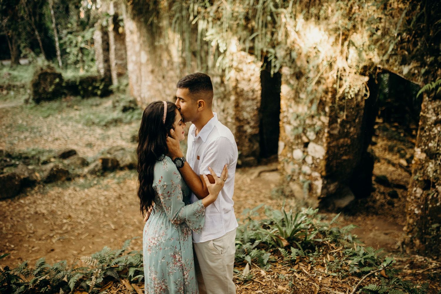 A romantic couple embraces among ancient stone ruins and hanging moss in a dreamy outdoor setting.