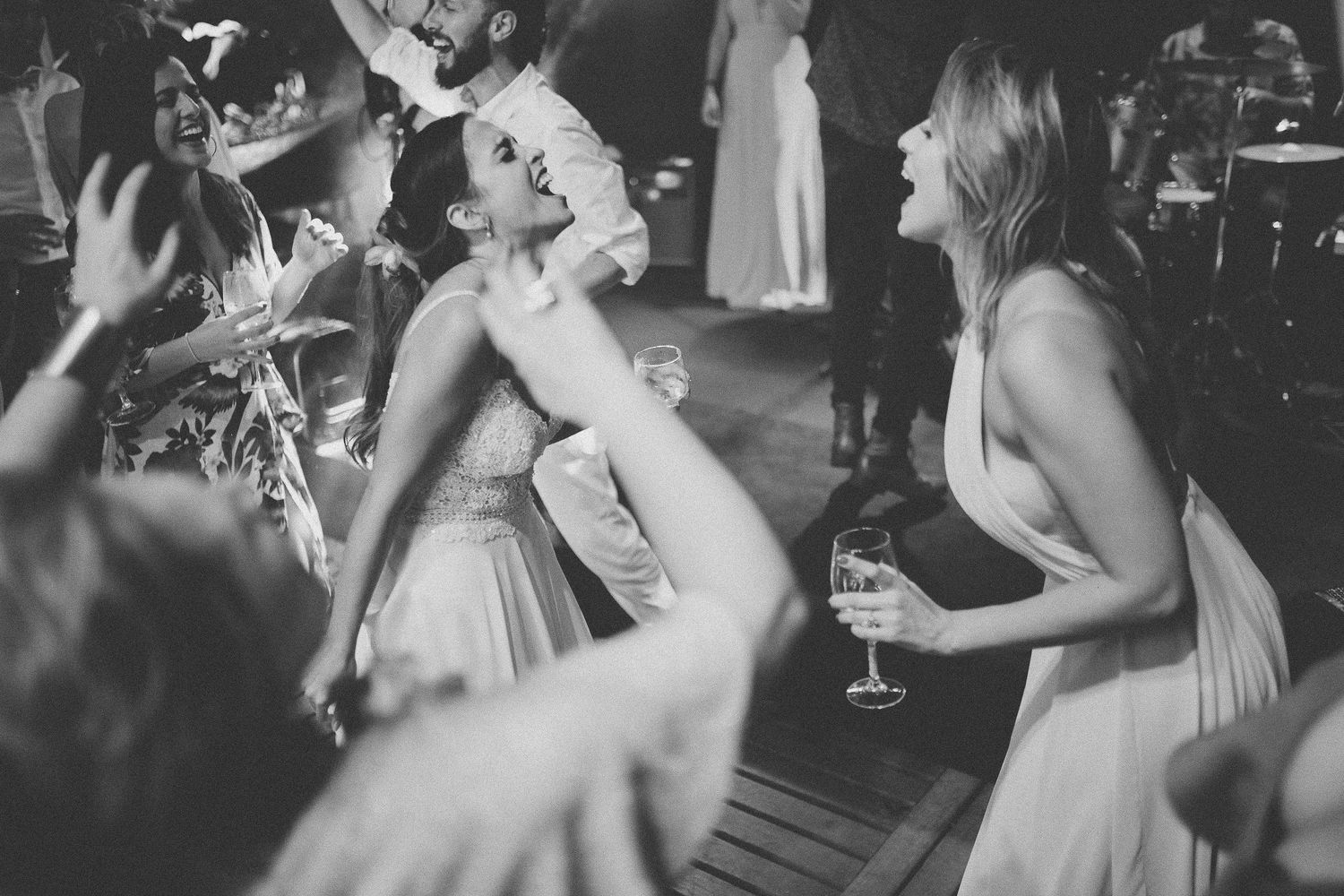 Black and white photo of wedding guests dancing and celebrating with drinks.