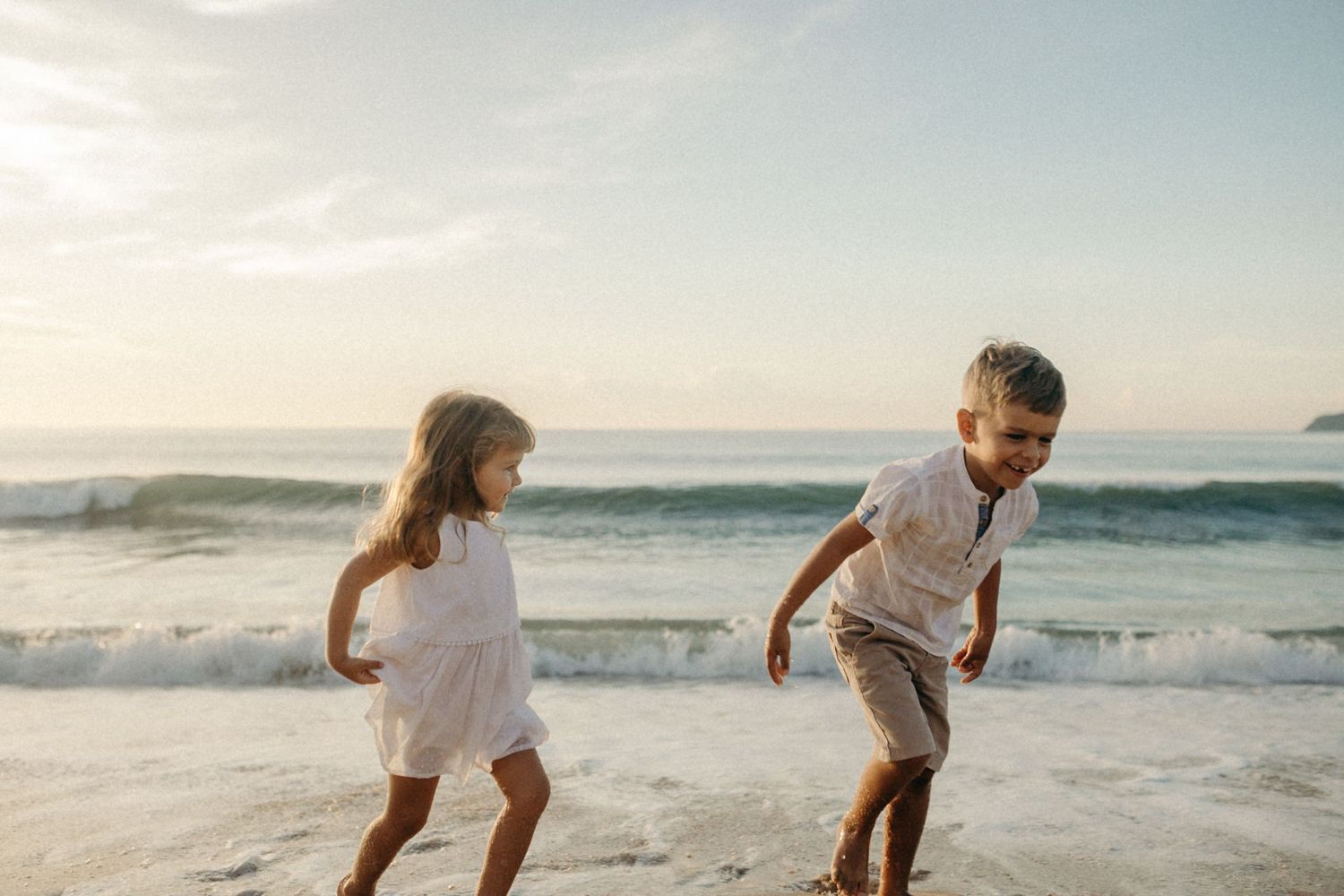 Two people playing and running on beach with ocean waves in background.