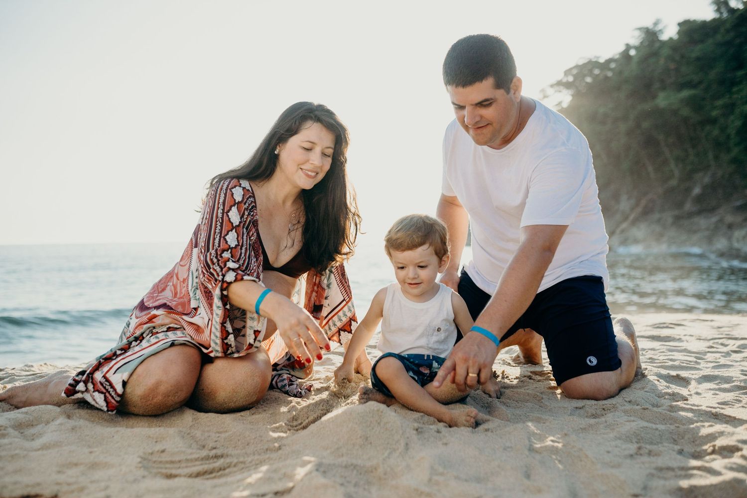 Family sitting together playing in sand on scenic beach at sunset.