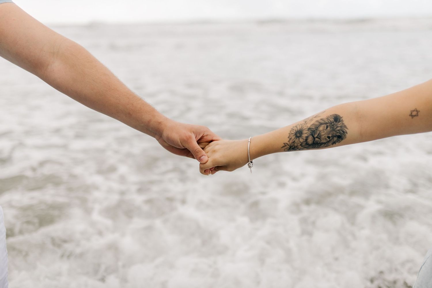 Two hands reach out to hold each other against a sandy beach background.