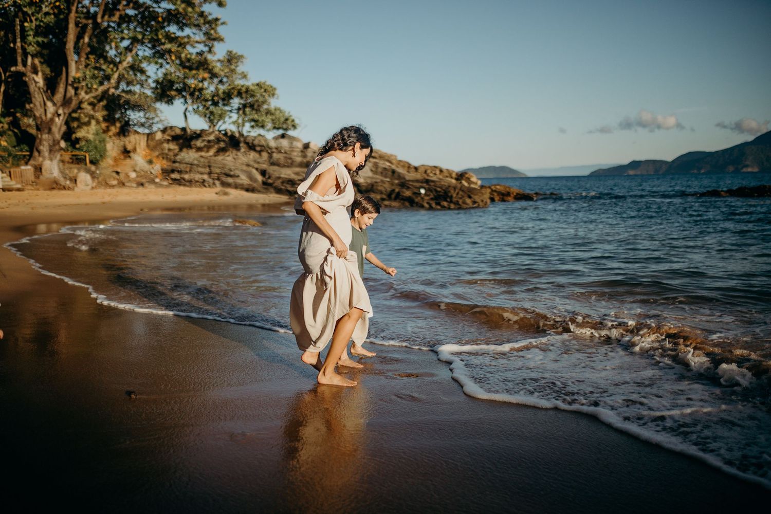Golden sunset light illuminates a sandy beach scene with gentle waves lapping at the shore.