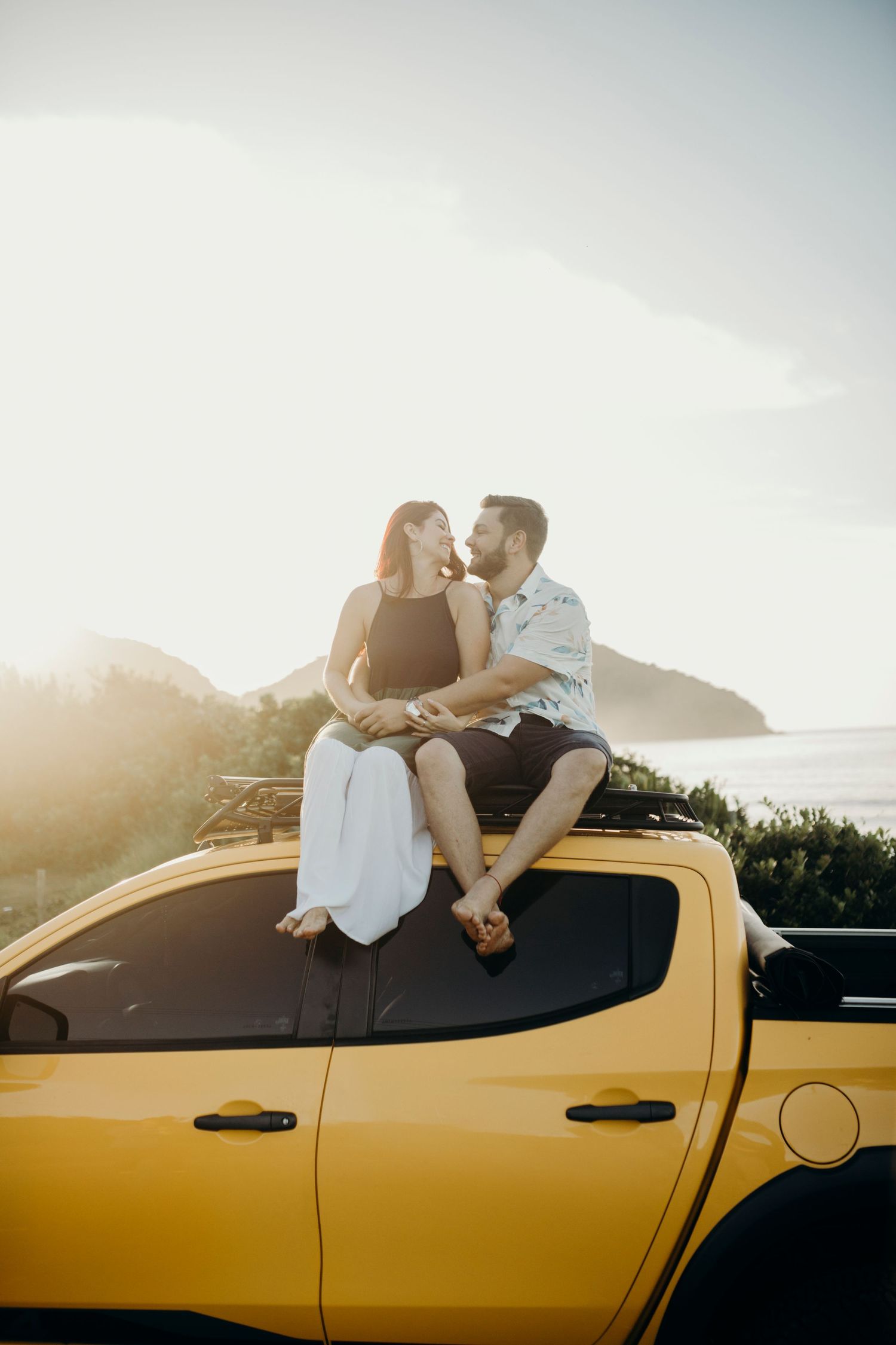 Romantic sunset moment on a yellow pickup truck overlooking coastal scenery.