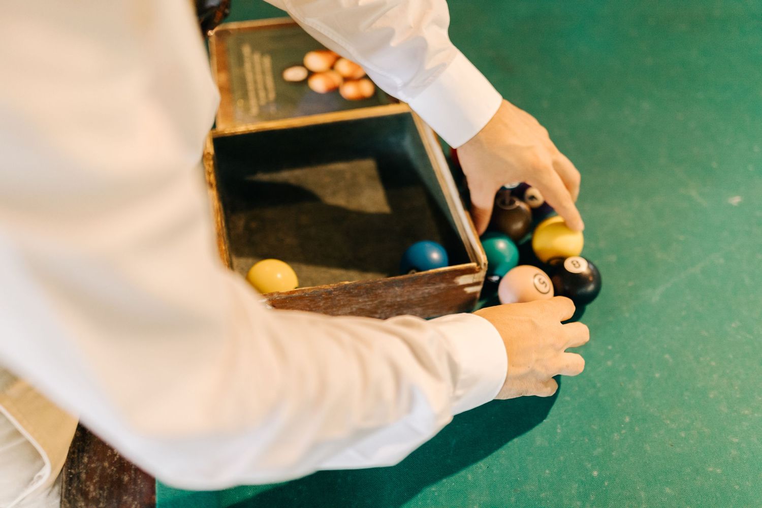 Hands playing with colorful pool balls on a green felt table surface.