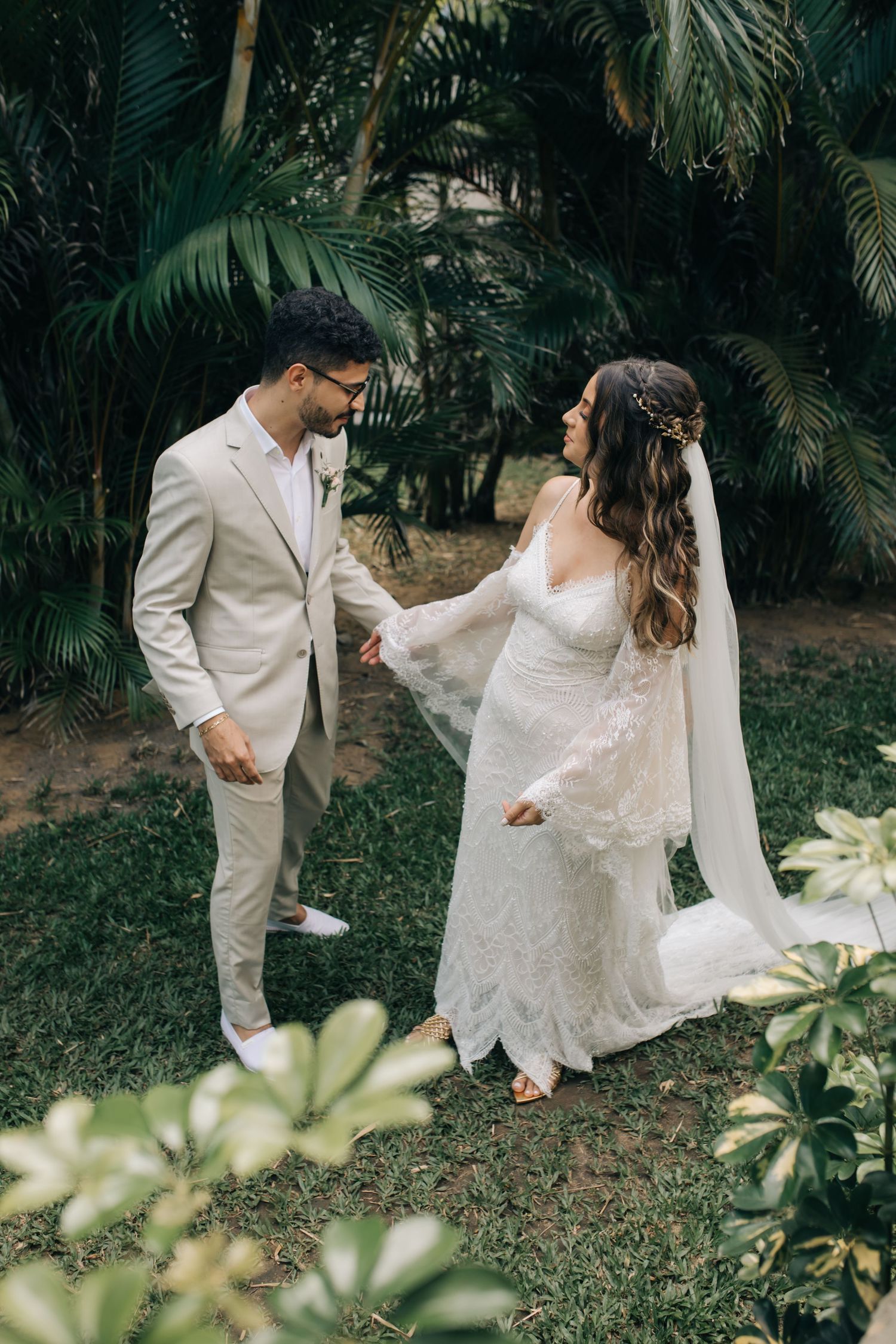 Tropical garden wedding scene with palm trees and couple in elegant white and beige attire.