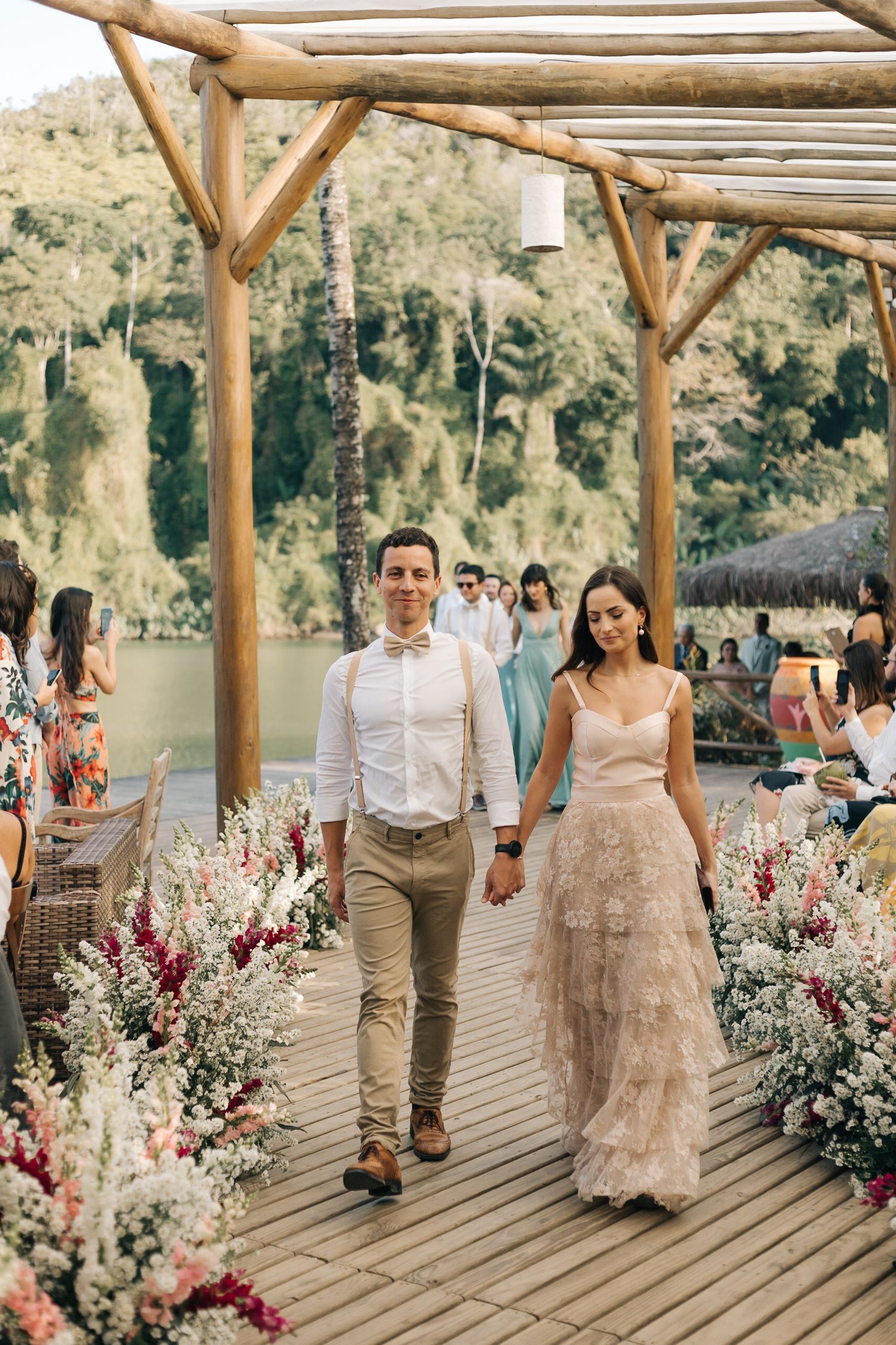 Couple walking down flower-lined wooden deck at outdoor event venue.