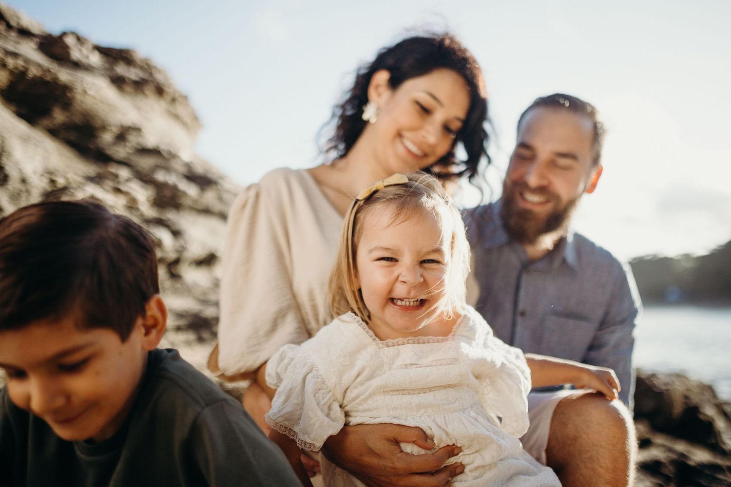 A heartwarming family scene unfolds on coastal rocks with ocean views in the background.