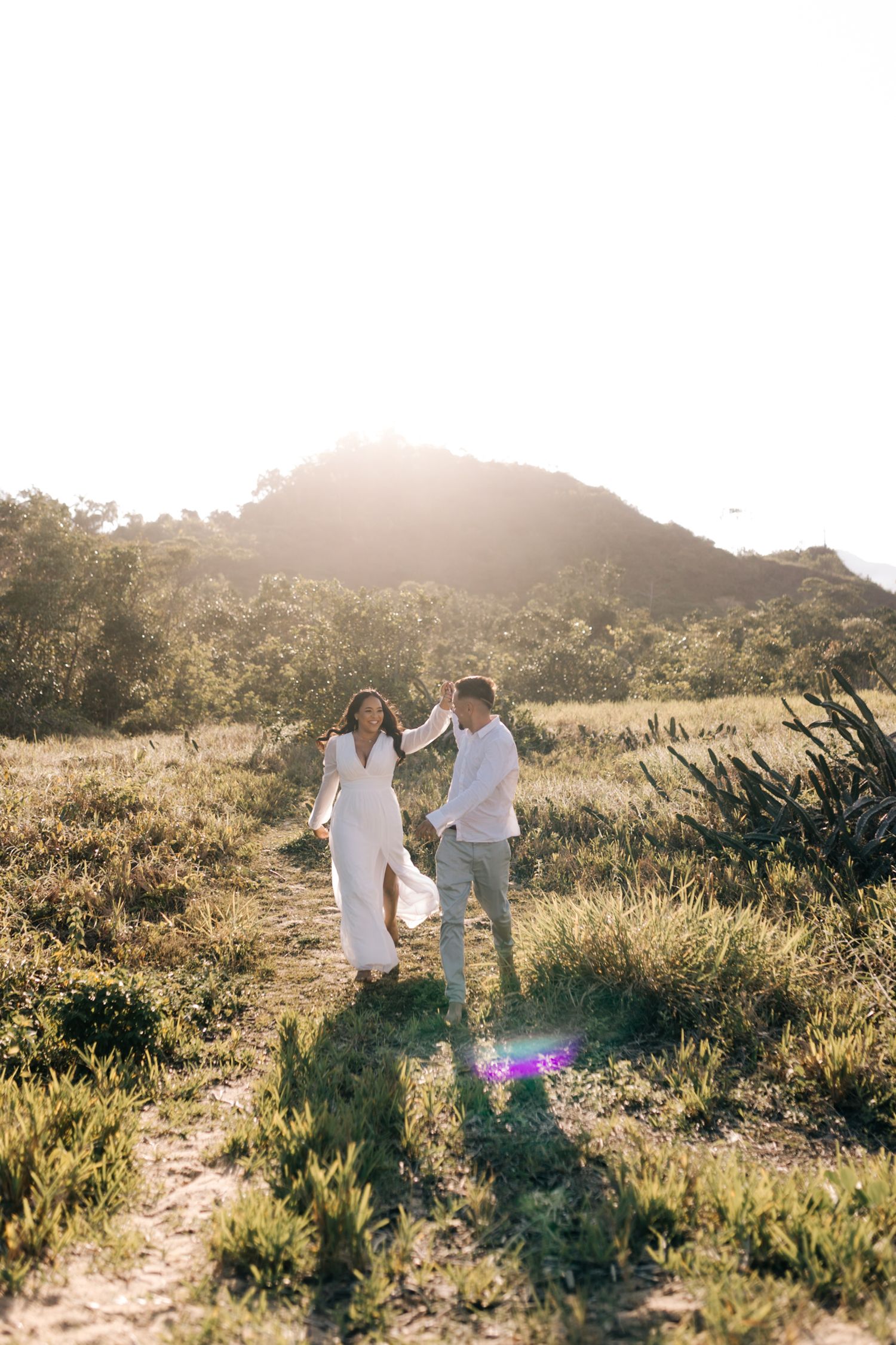 A couple holds hands while walking together on a scenic mountain path at sunset.