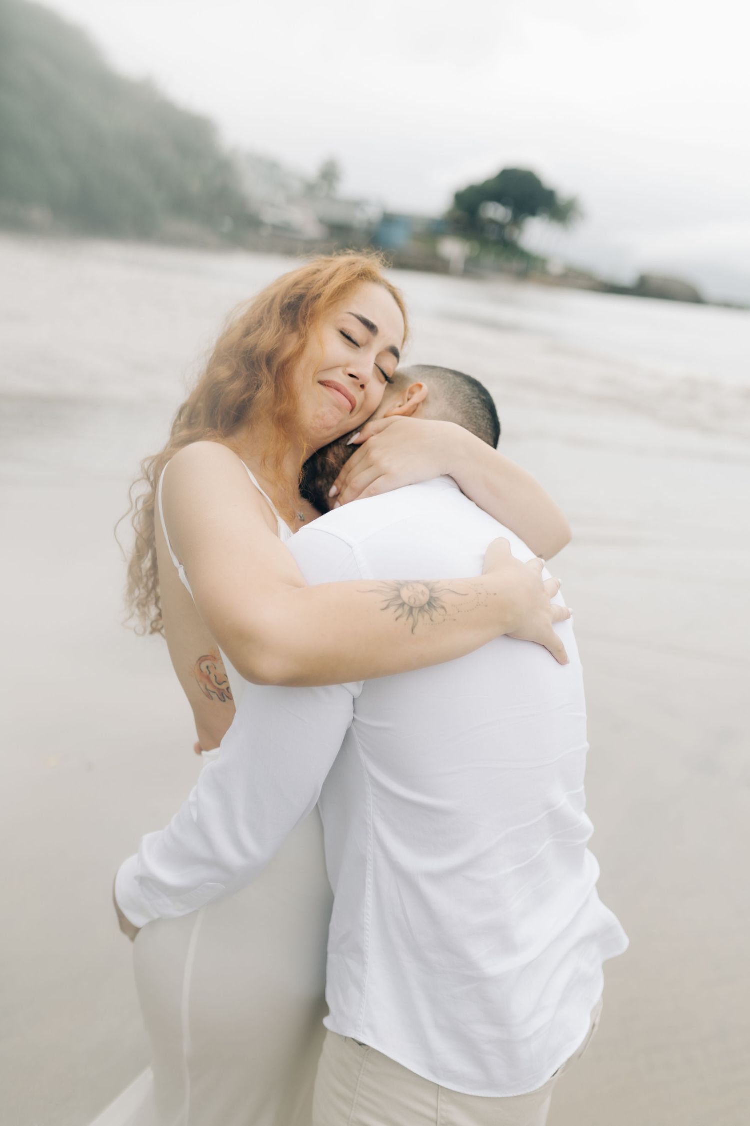 A romantic embrace captured on a foggy beach with soft, dreamy lighting.