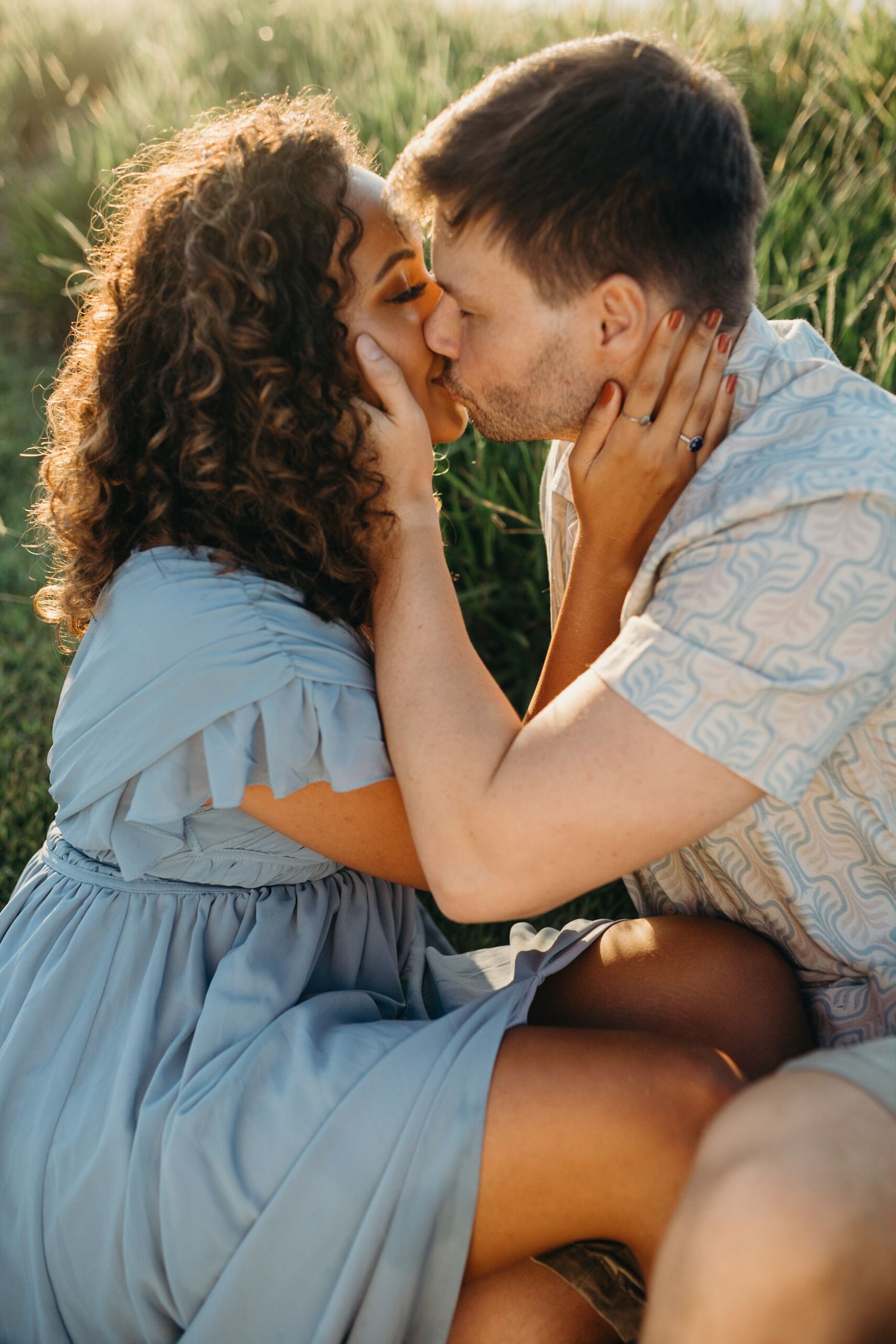Romantic couple in blue and white sharing intimate kiss in grassy field.