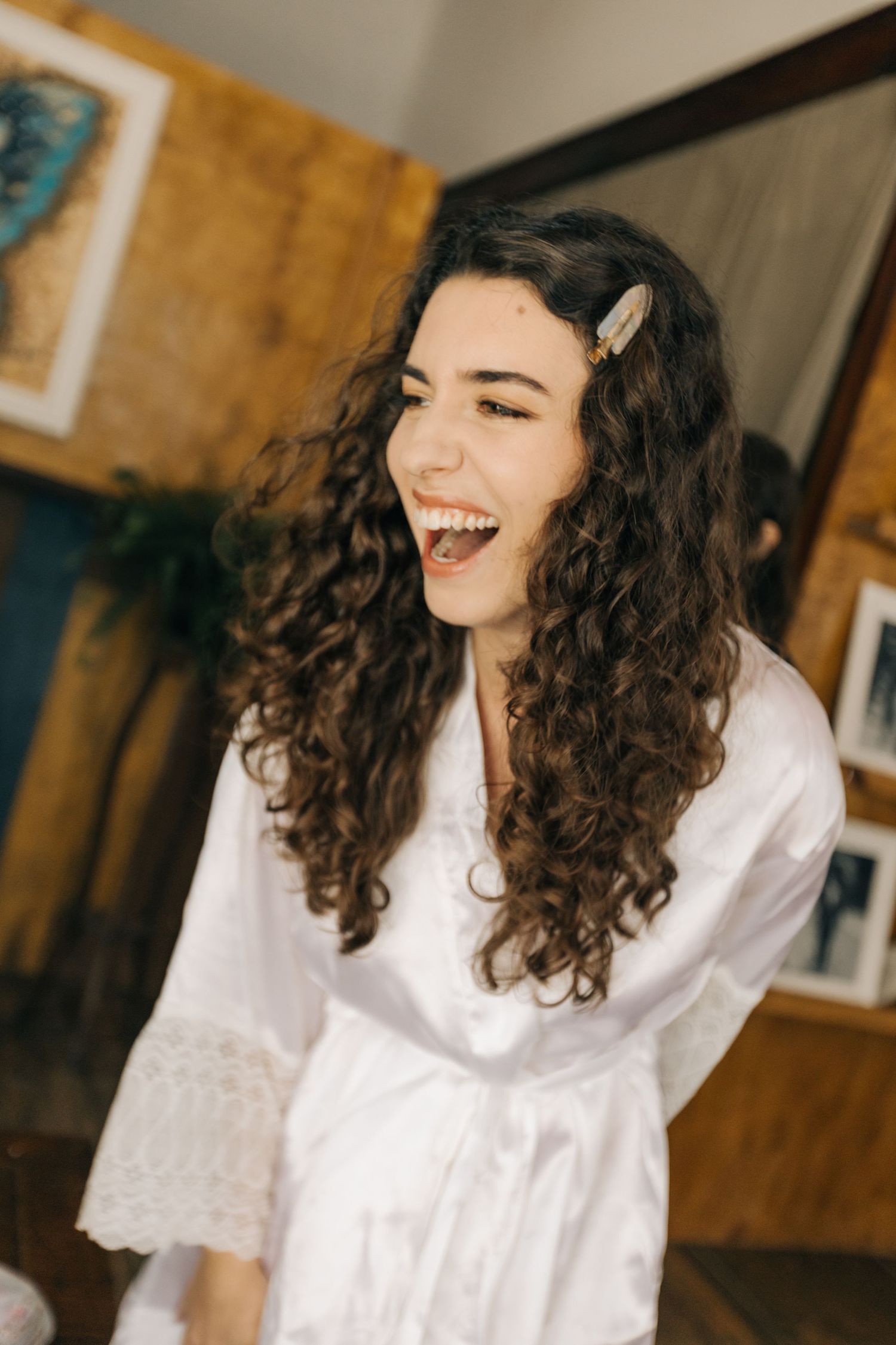 Candid portrait of woman in white robe laughing with curly hair and hair accessories.