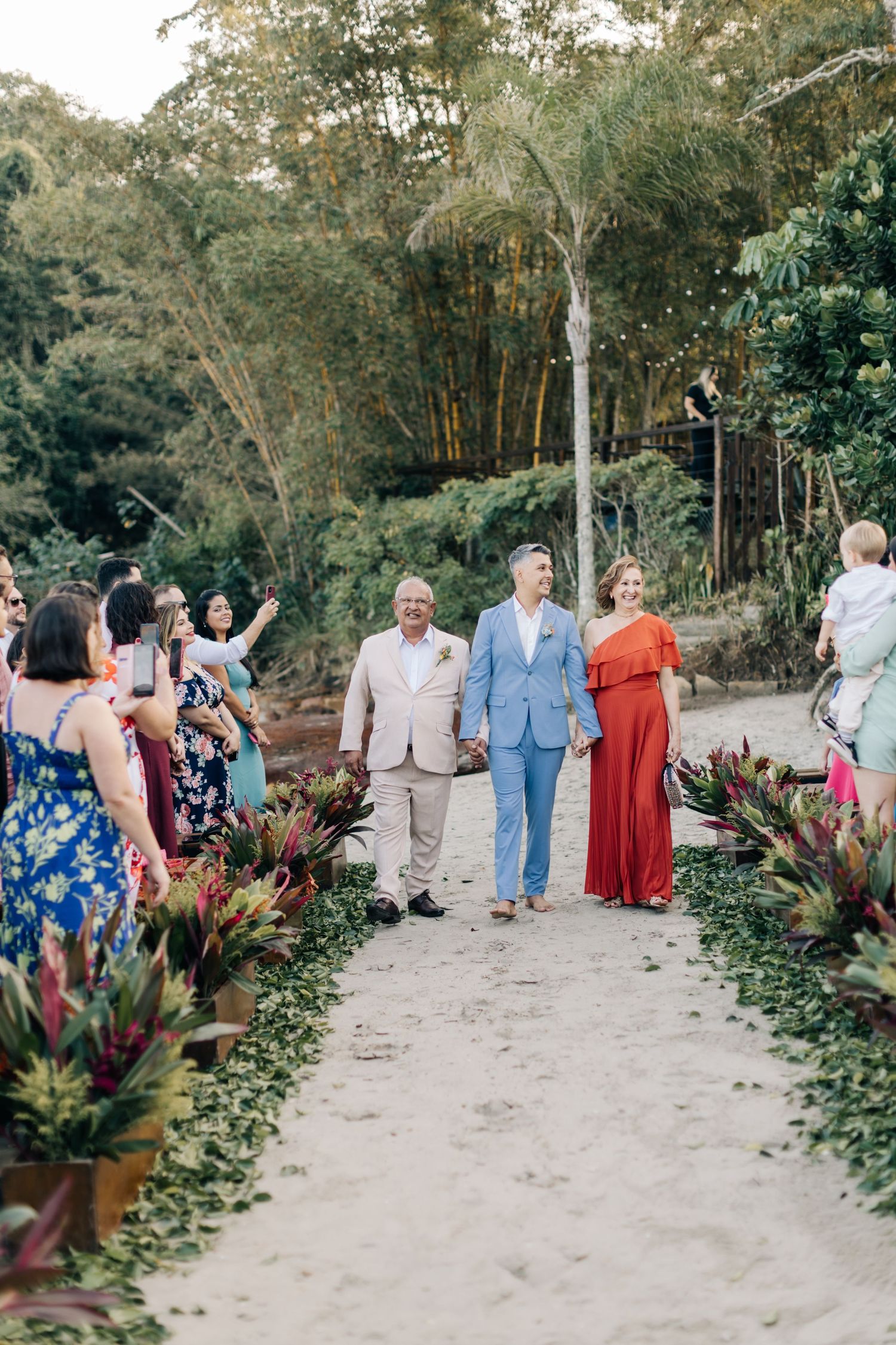 Wedding party walking down a tropical garden path lined with colorful plants and guests.