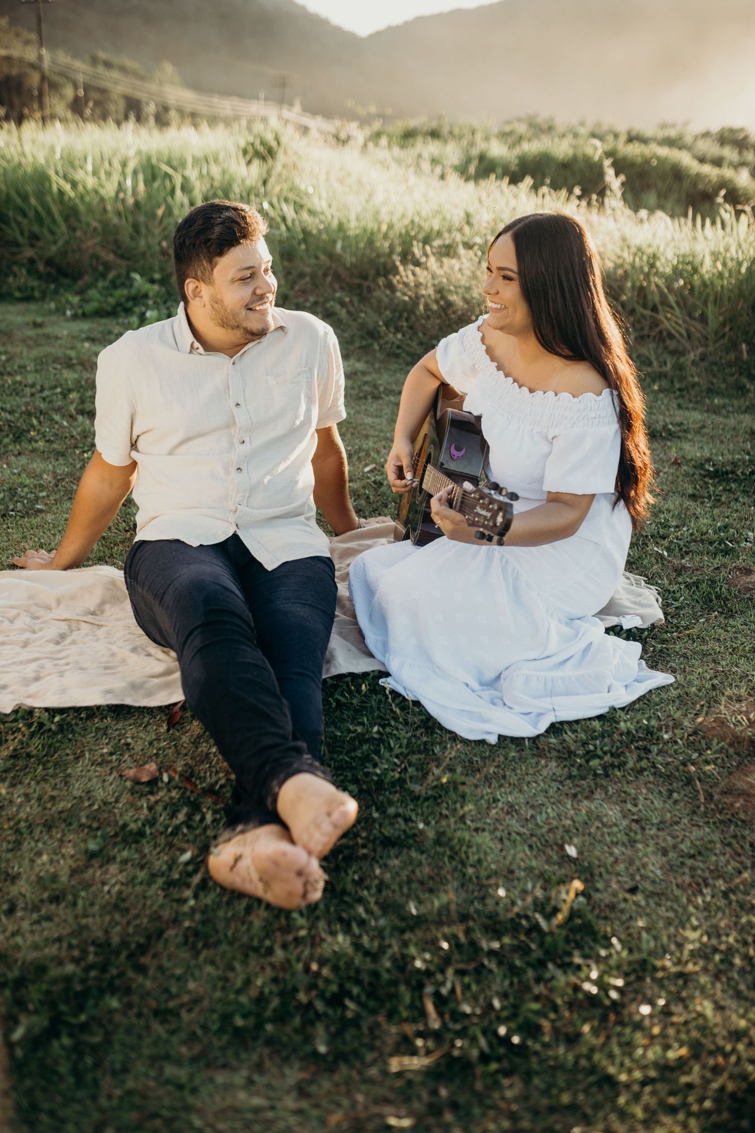 Candid moment of couple sitting on blanket in grassy field during golden hour.