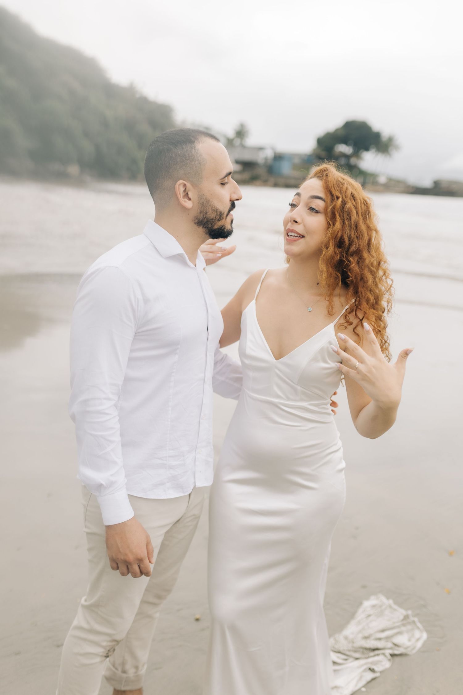 A romantic couple in white outfits shares a joyful moment together on a misty beach.