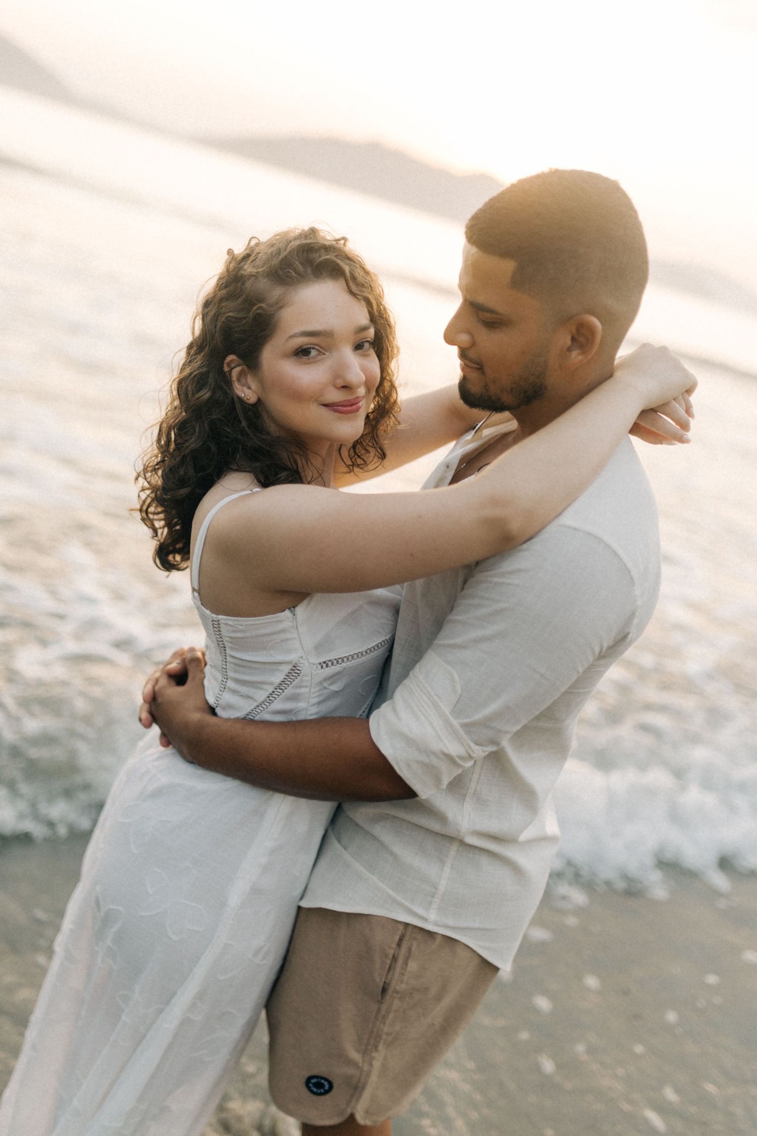Happy couple sharing tender moment on beach with soft sunset lighting.