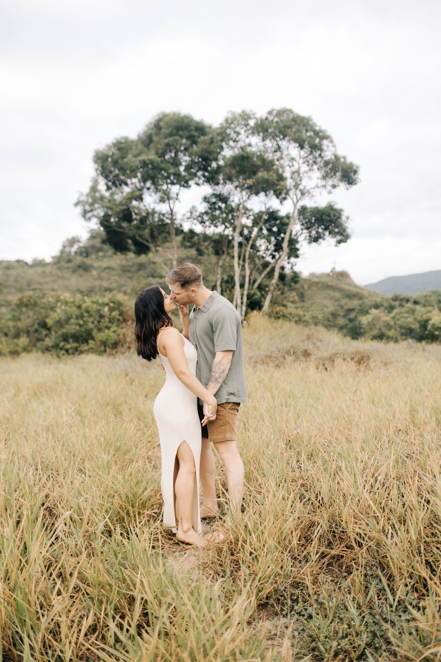 A couple shares an intimate moment in a golden field with trees in the background.
