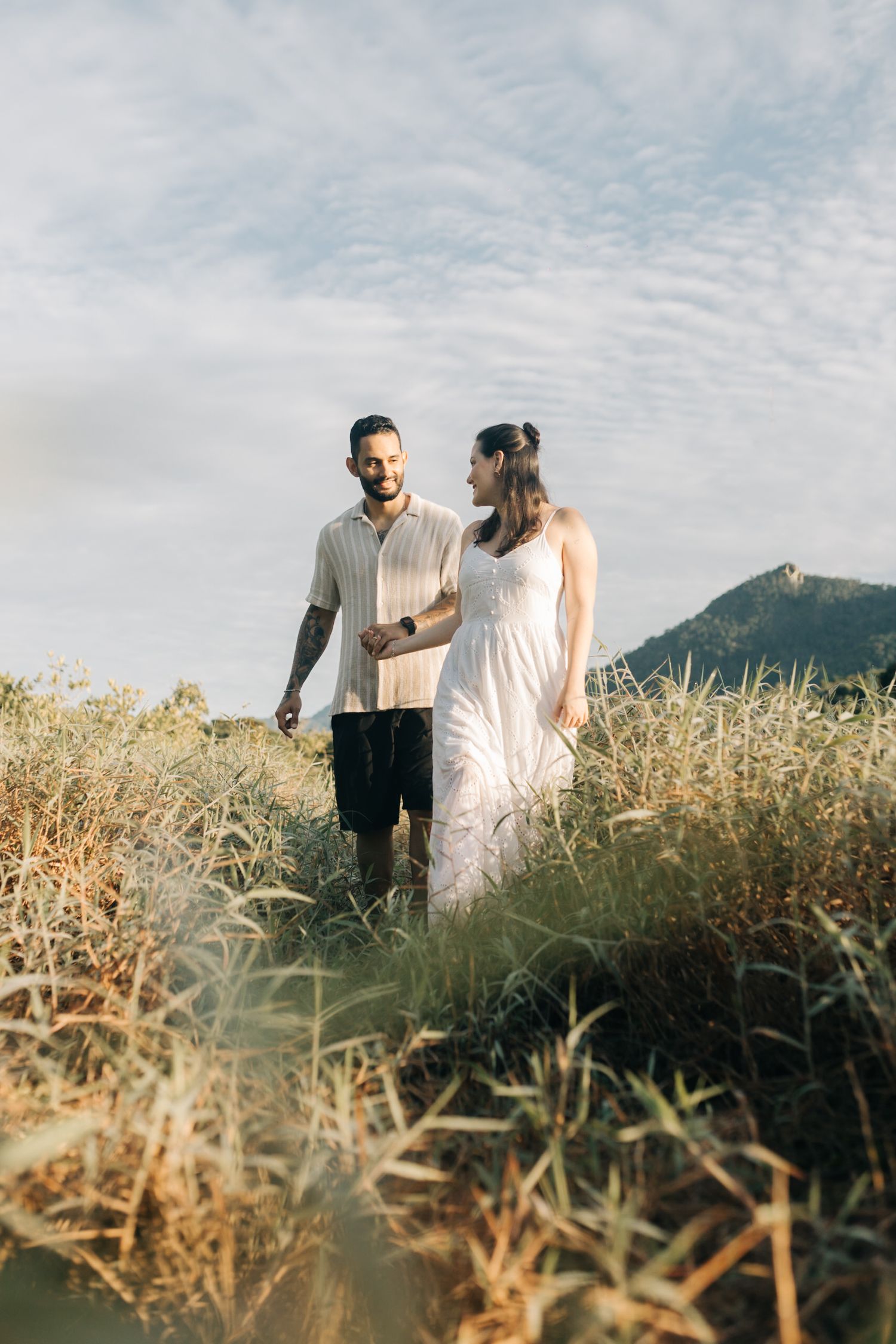 A couple walks through tall dry grass with mountains visible in background.
