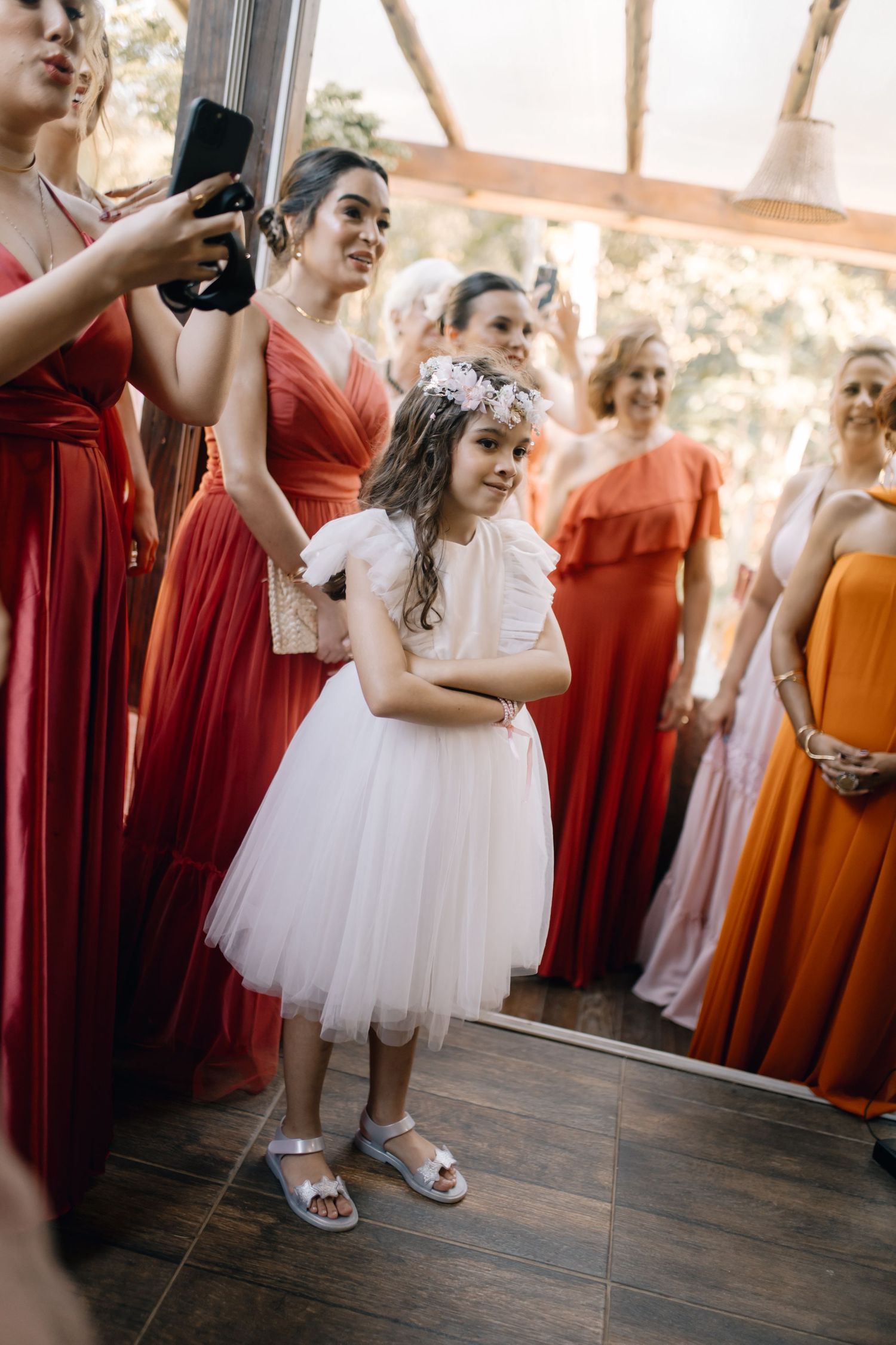 Young attendant in white tulle dress poses while surrounded by bridesmaids in coral gowns.