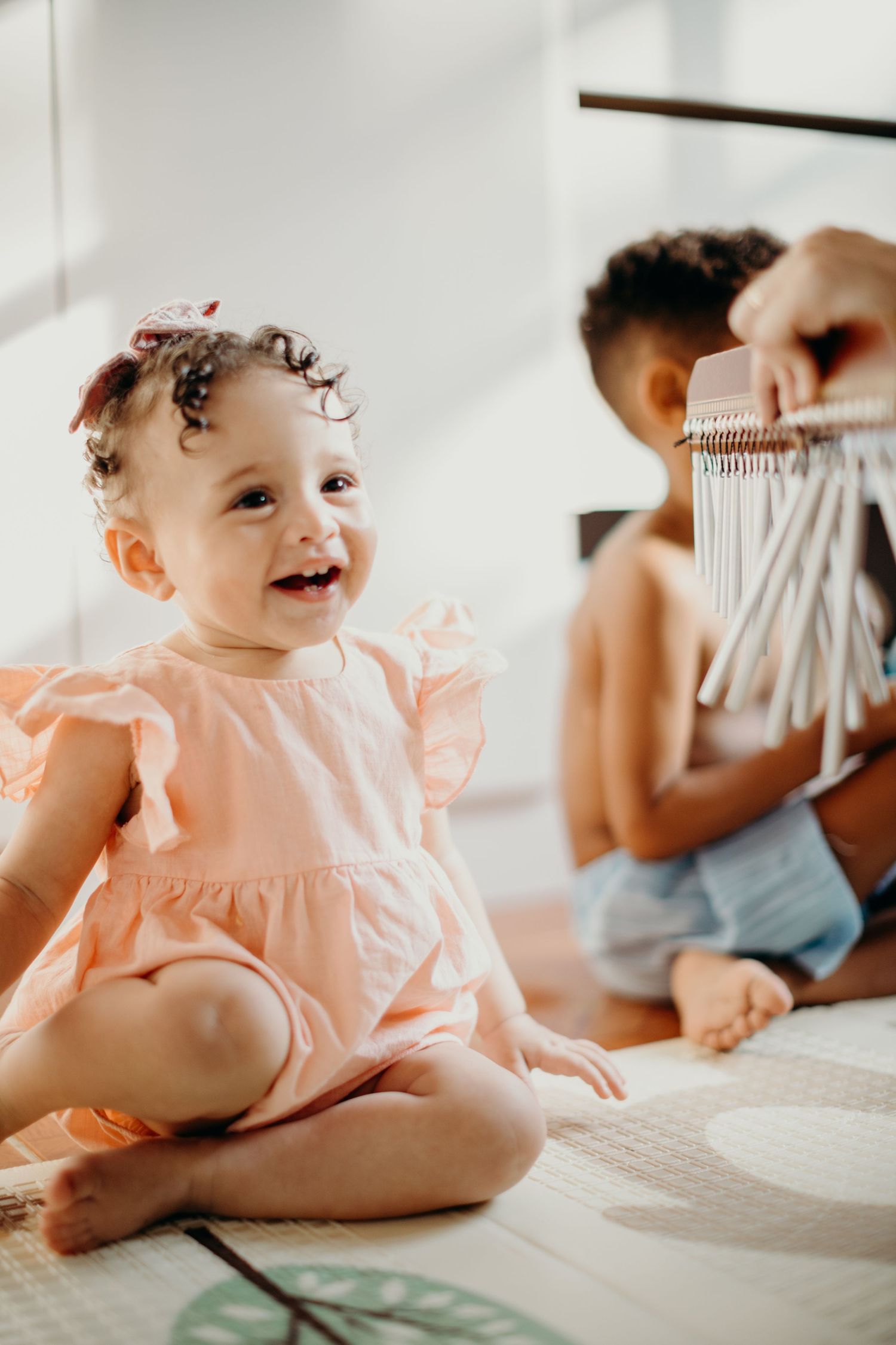 A happy baby in a peach dress sitting during a music activity.