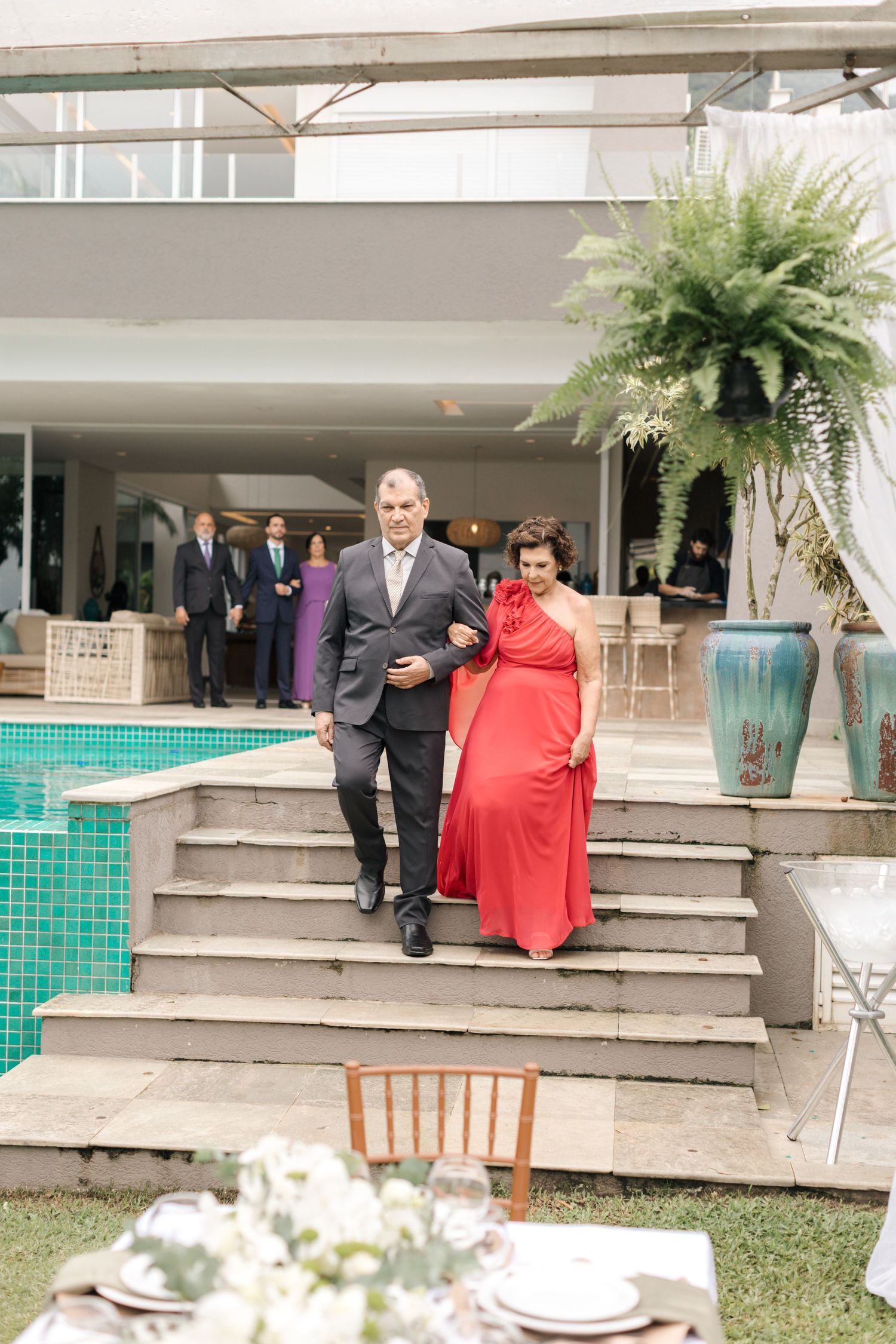 Pair walking down outdoor steps in formal attire by swimming pool.