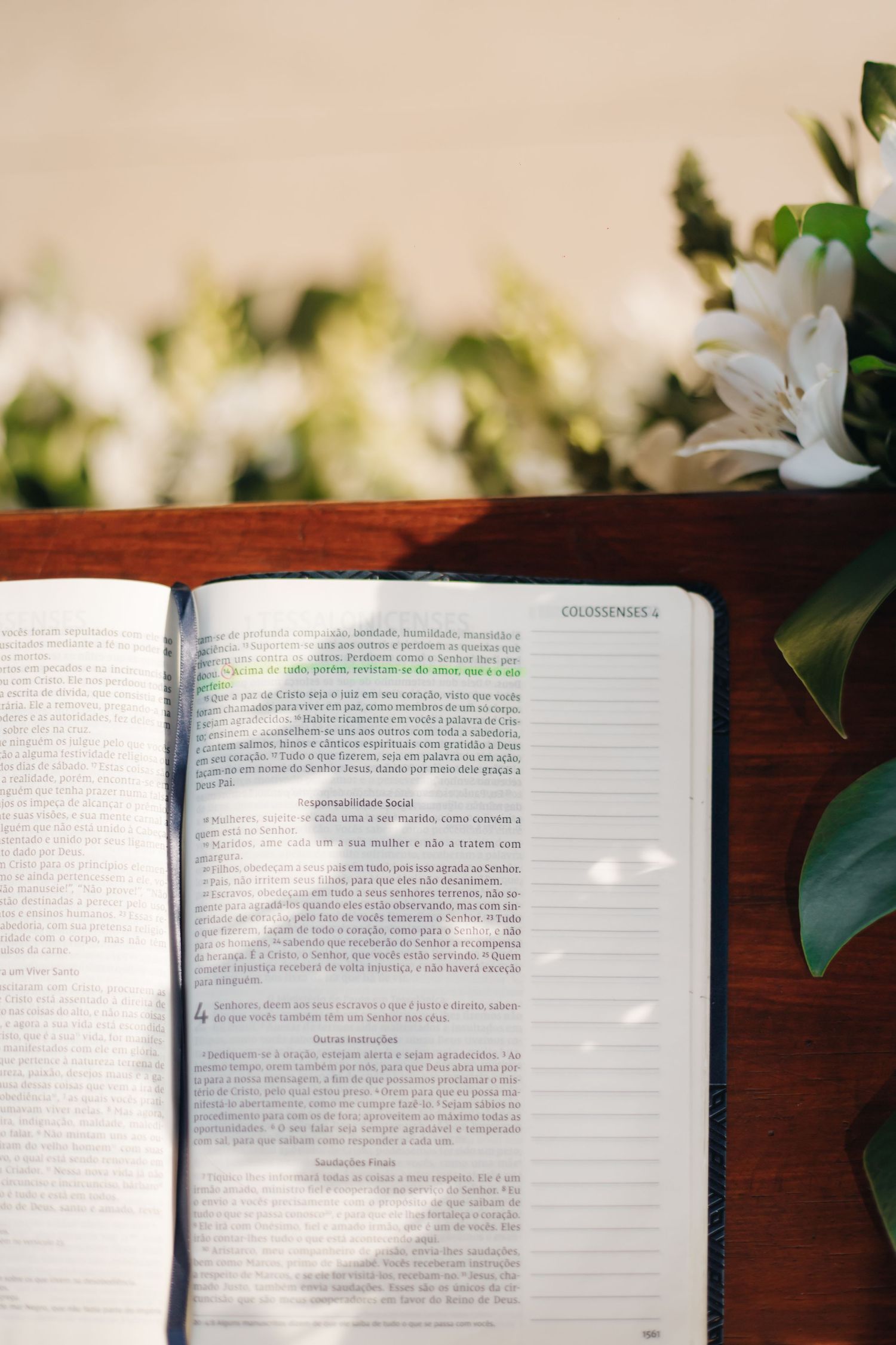 An open Bible on wooden surface with white lilies and greenery in soft natural light.