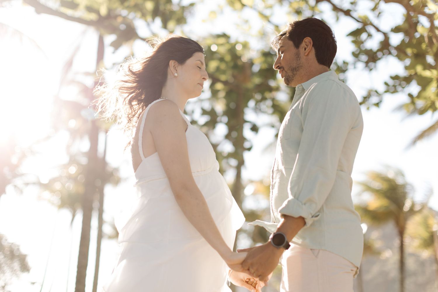 A couple shares a romantic moment outdoors with palm trees and sunlight creating a dreamy atmosphere.
