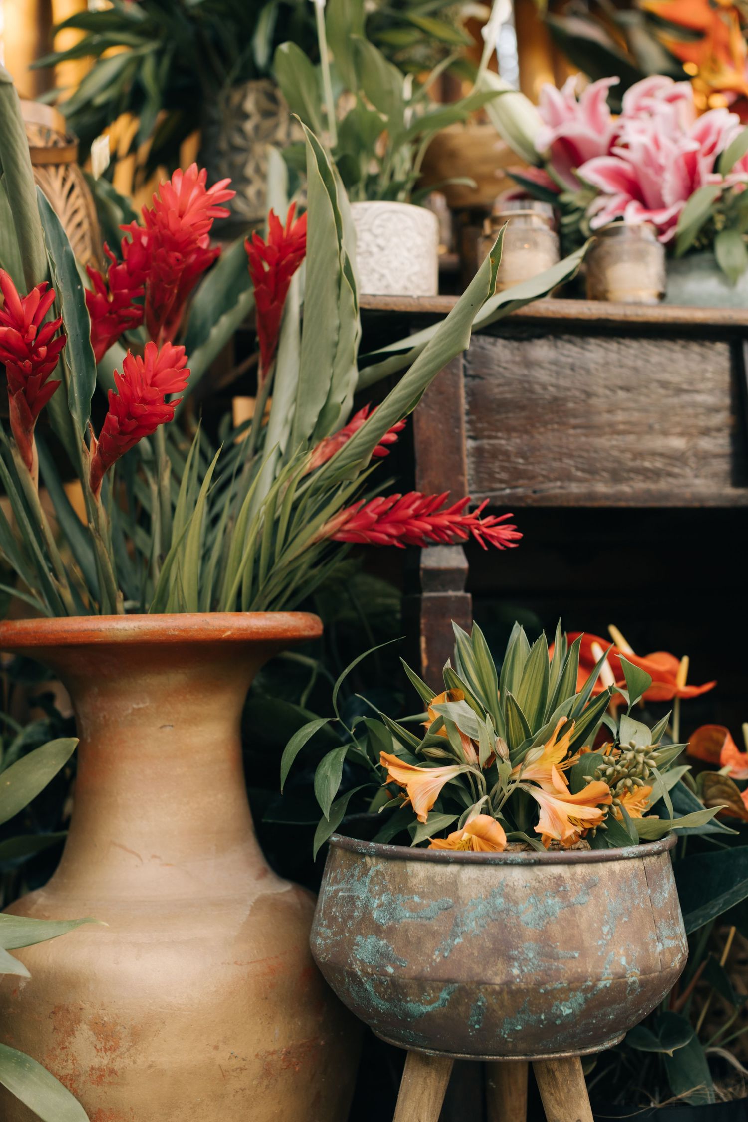 Red ginger flowers and orange blooms arranged in clay vase and patinated copper planter.