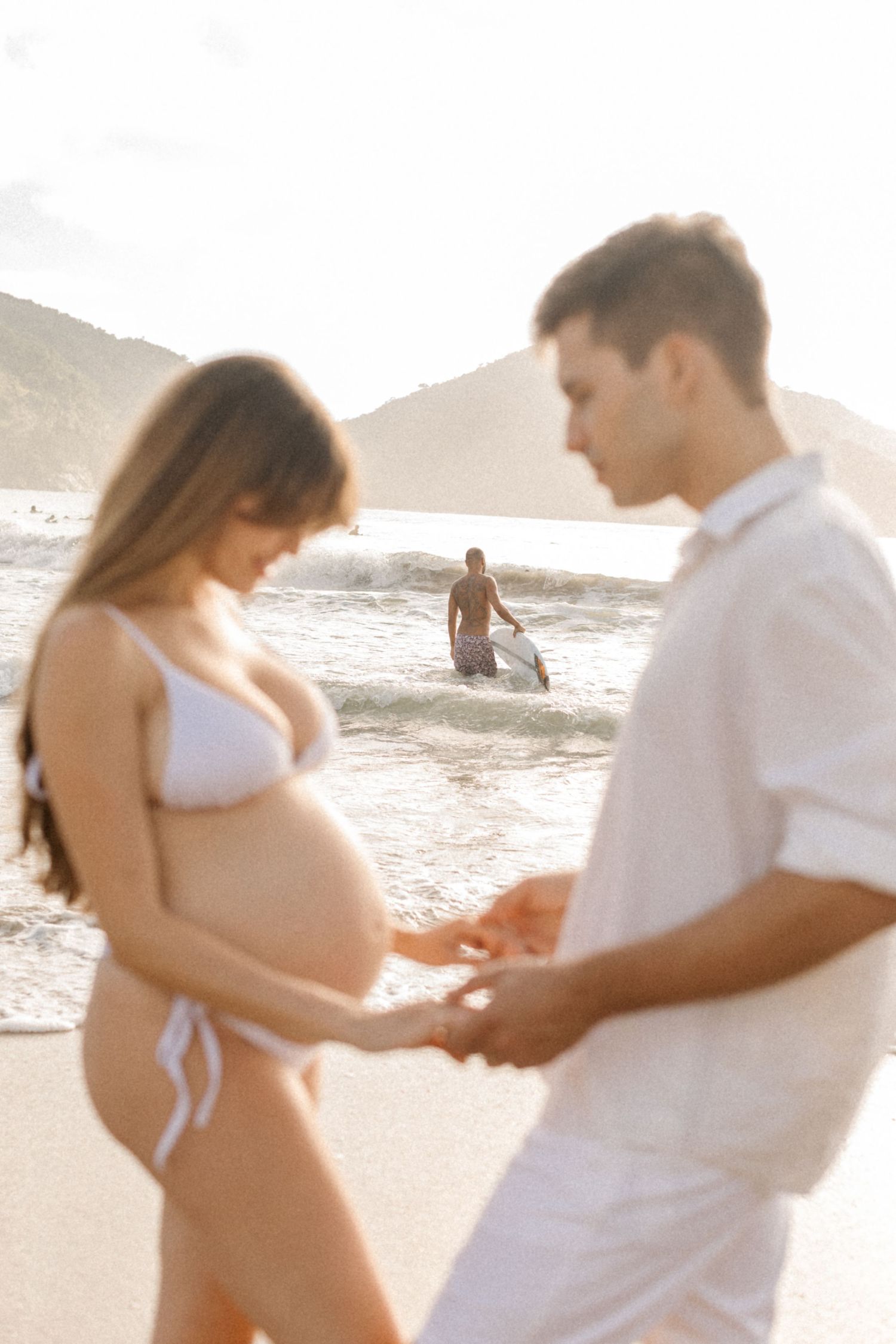 Intimate beach photoshoot of an expecting couple in white attire.
