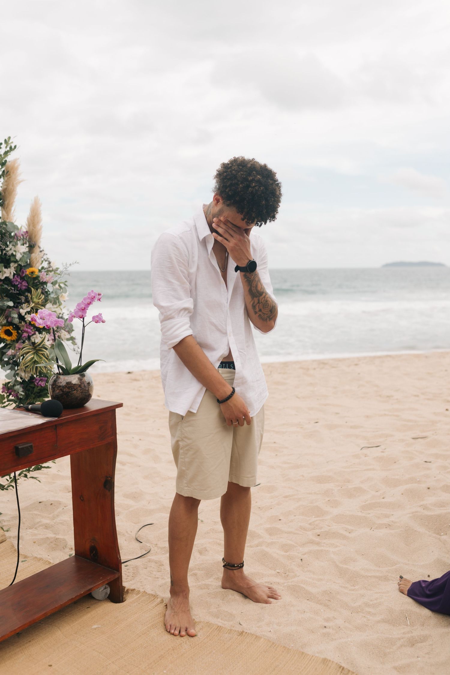 An emotional moment during a beach wedding with floral decorations and ocean views.