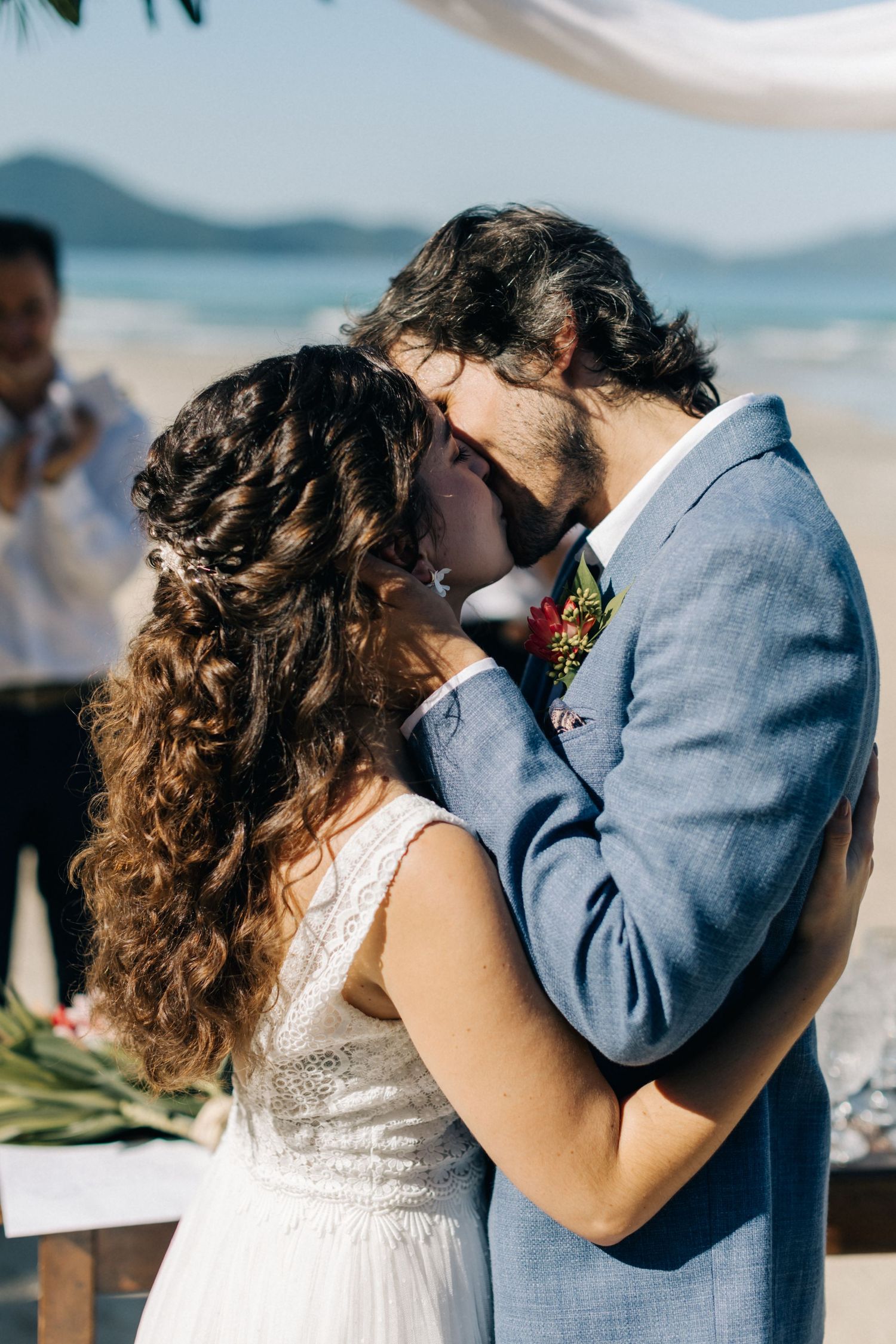 Emotional wedding ceremony moment on sandy beach with ocean backdrop.