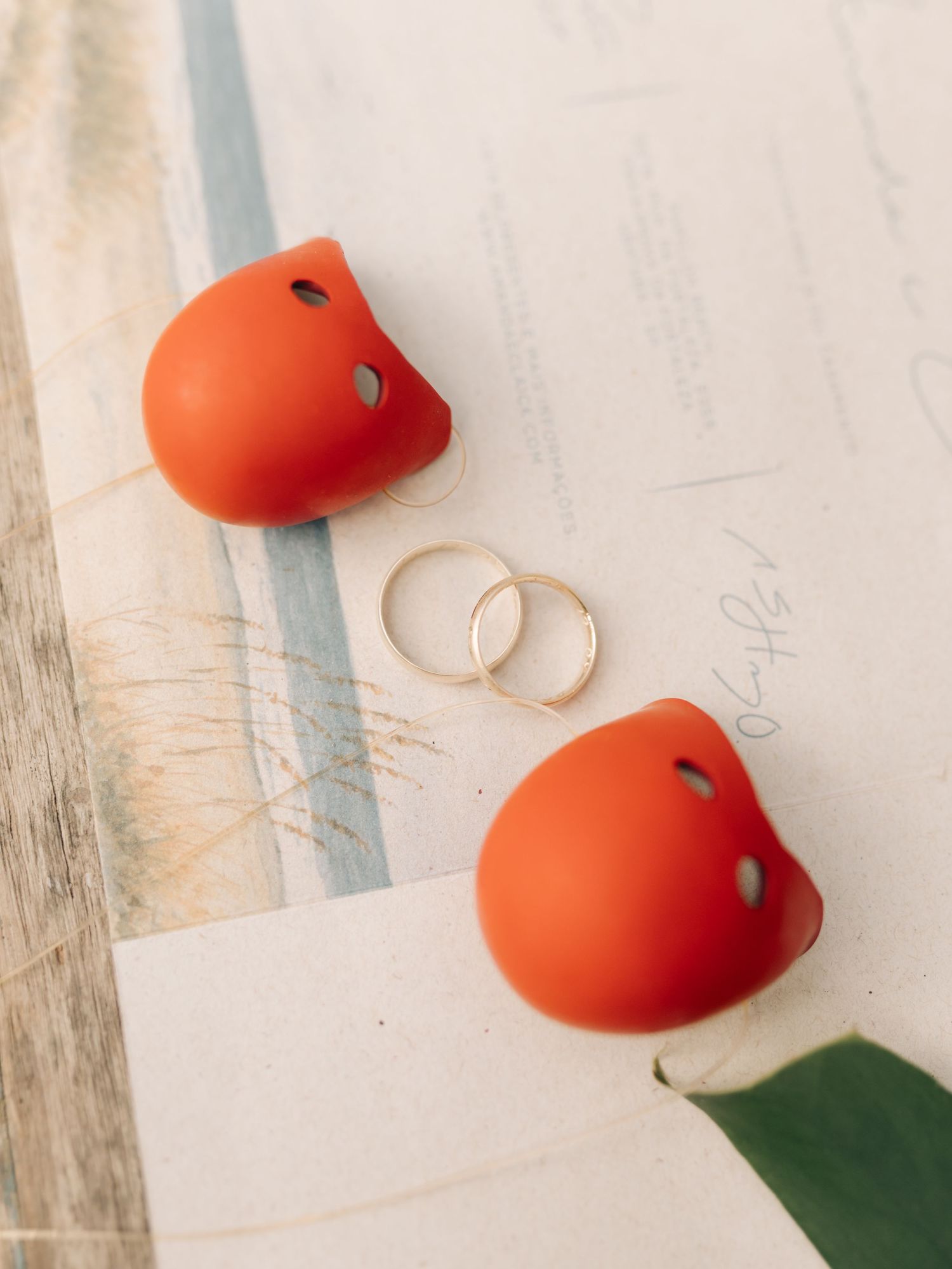 Wedding rings placed between two orange heart decorations on white paper.